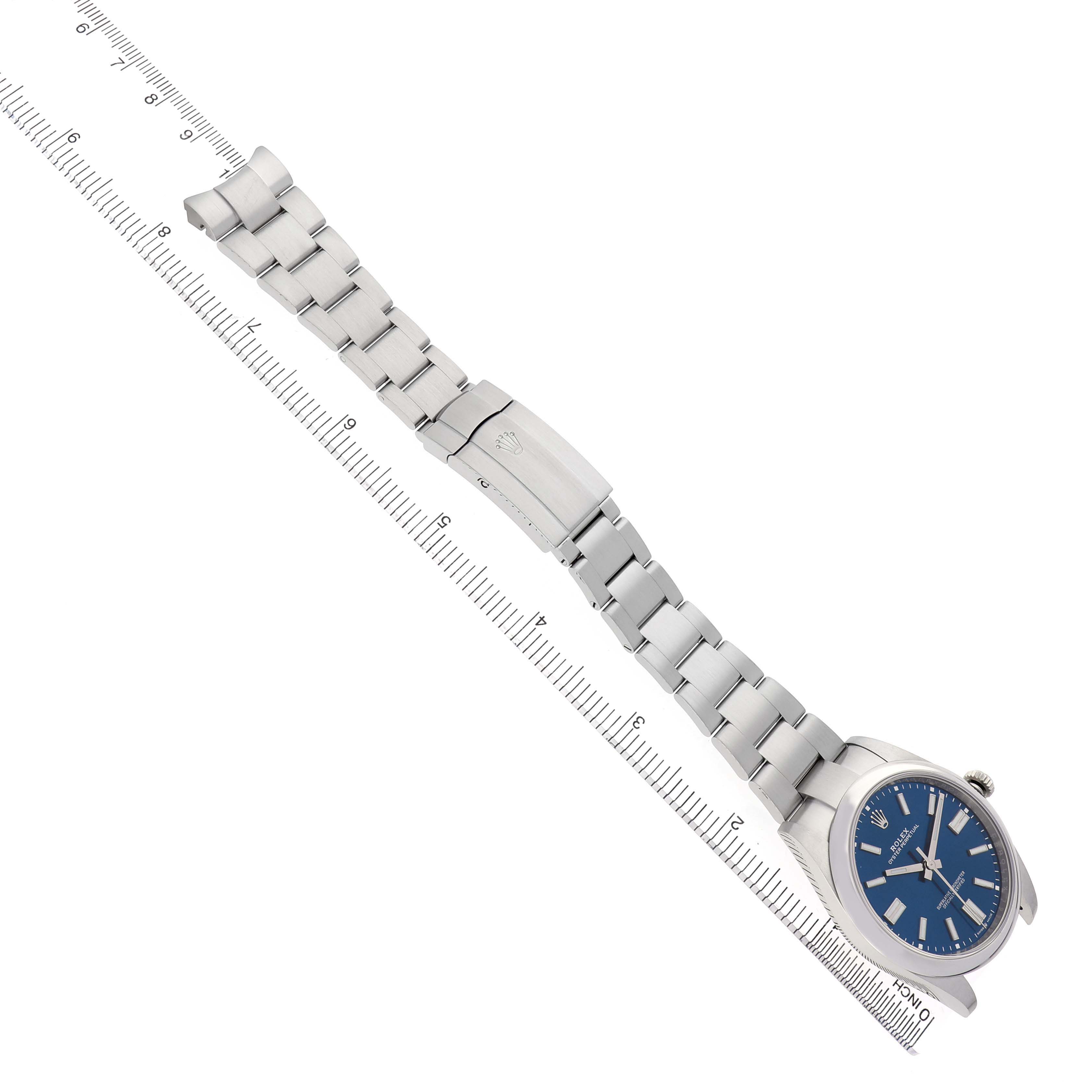 The Rolex Oyster Perpetual 124300 Men's Stainless Steel Blue Dial watch is shown from a top-down angle, with the face and full bracelet visible next to a ruler.