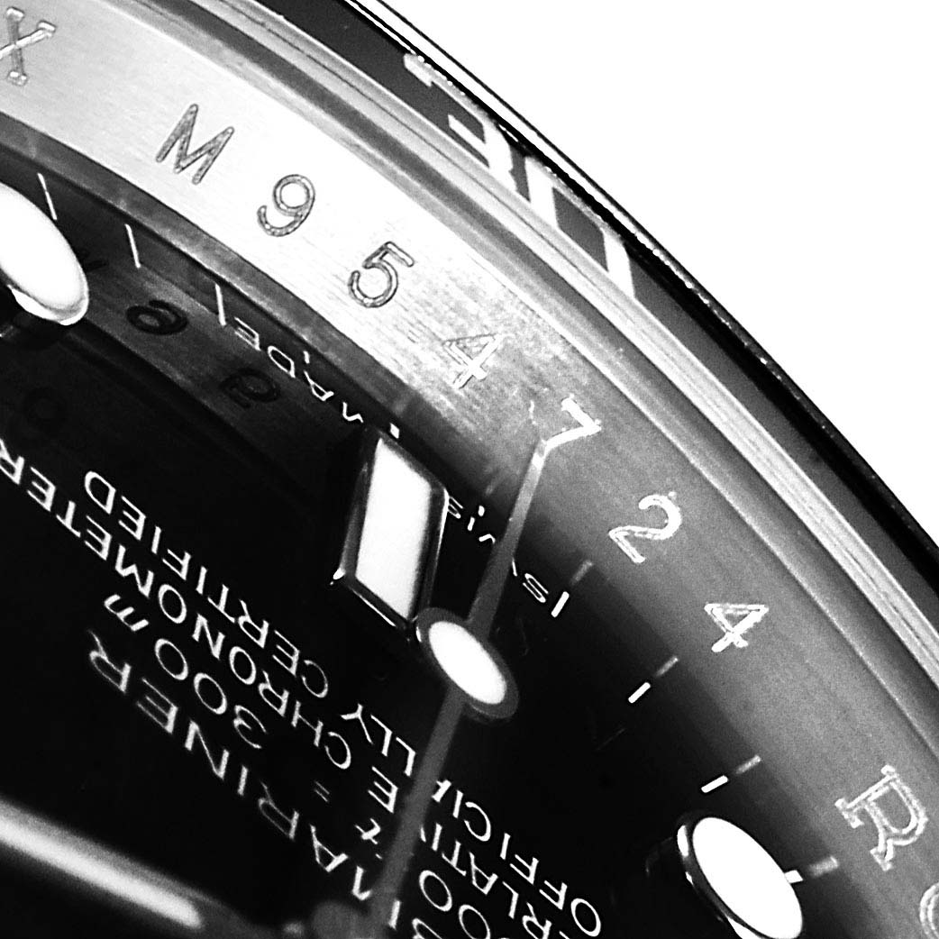 This close-up image of a Rolex Submariner 14060M Men
s Stainless Steel Black Dial 14060M Men
s Stainless Steel Black Dial watch shows part of the dial, chapter ring with serial number, and minute markers.