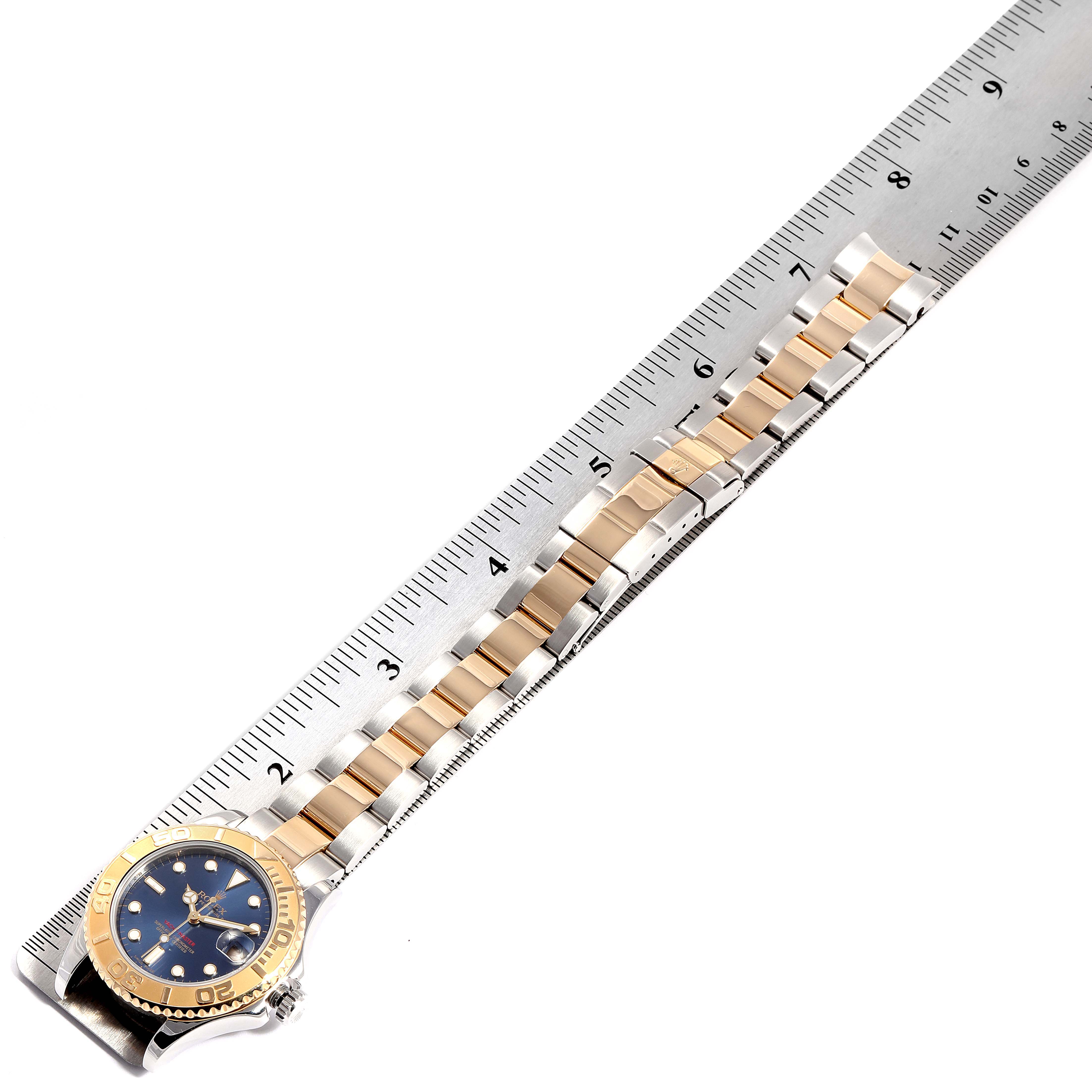 The Rolex Yacht-Master 168623 Men's Steel and Gold (two tone) Blue Dial 168623 Men's Steel and Gold (two tone) Blue Dial watch is shown from the top view with a metal ruler beside it, displaying its bracelet and dial.