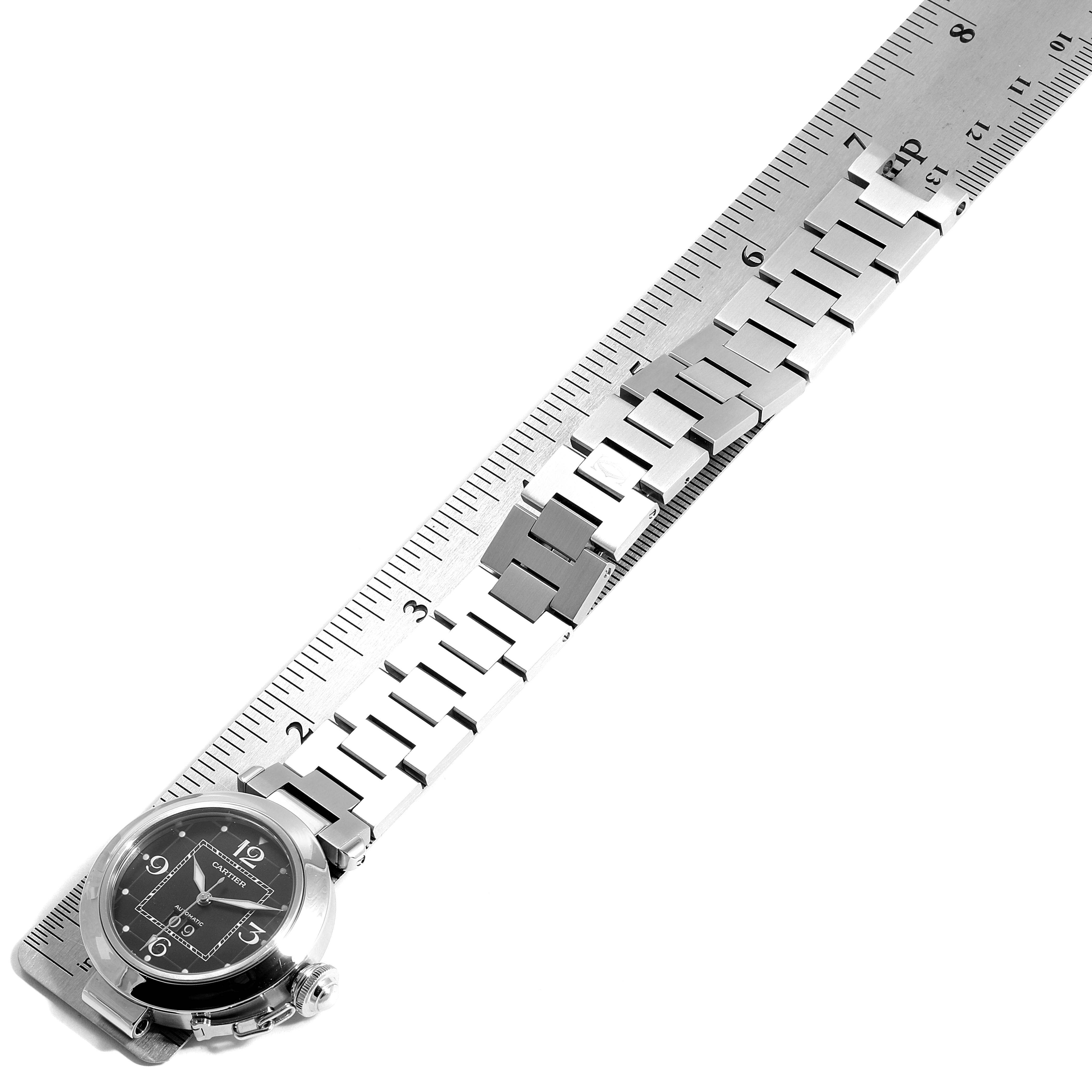 The Cartier Pasha W31053M7 Women's Stainless Steel Black Dial W31053M7 Women's Stainless Steel Black Dial watch is shown from a top-down angle, featuring its dial and metallic bracelet alongside a ruler for scale.