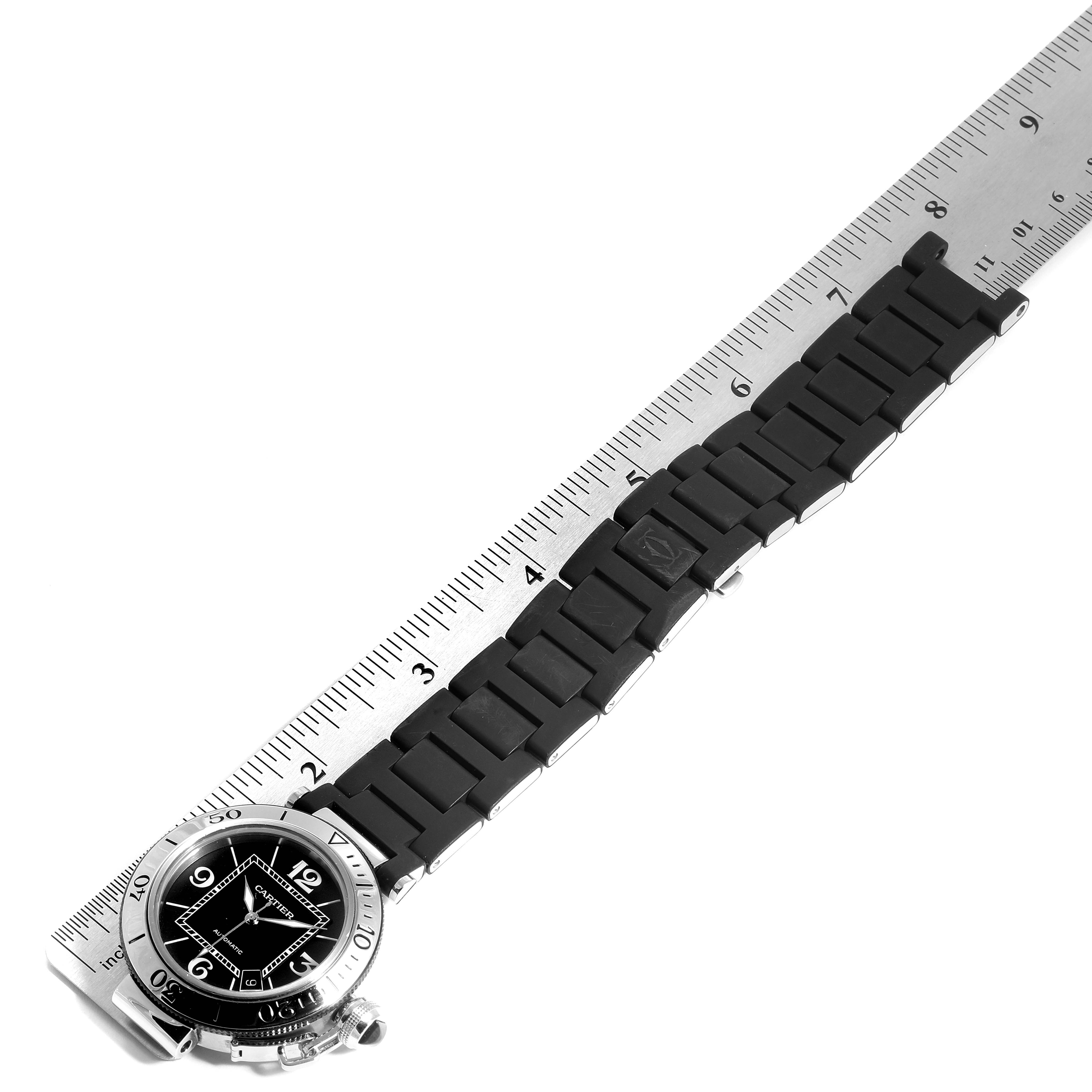 The image shows the Cartier Pasha W31088U2 Men
s Stainless Steel Black Dial W31088U2 Men
s Stainless Steel Black Dial watch laid flat next to a ruler, highlighting the watch face and band.