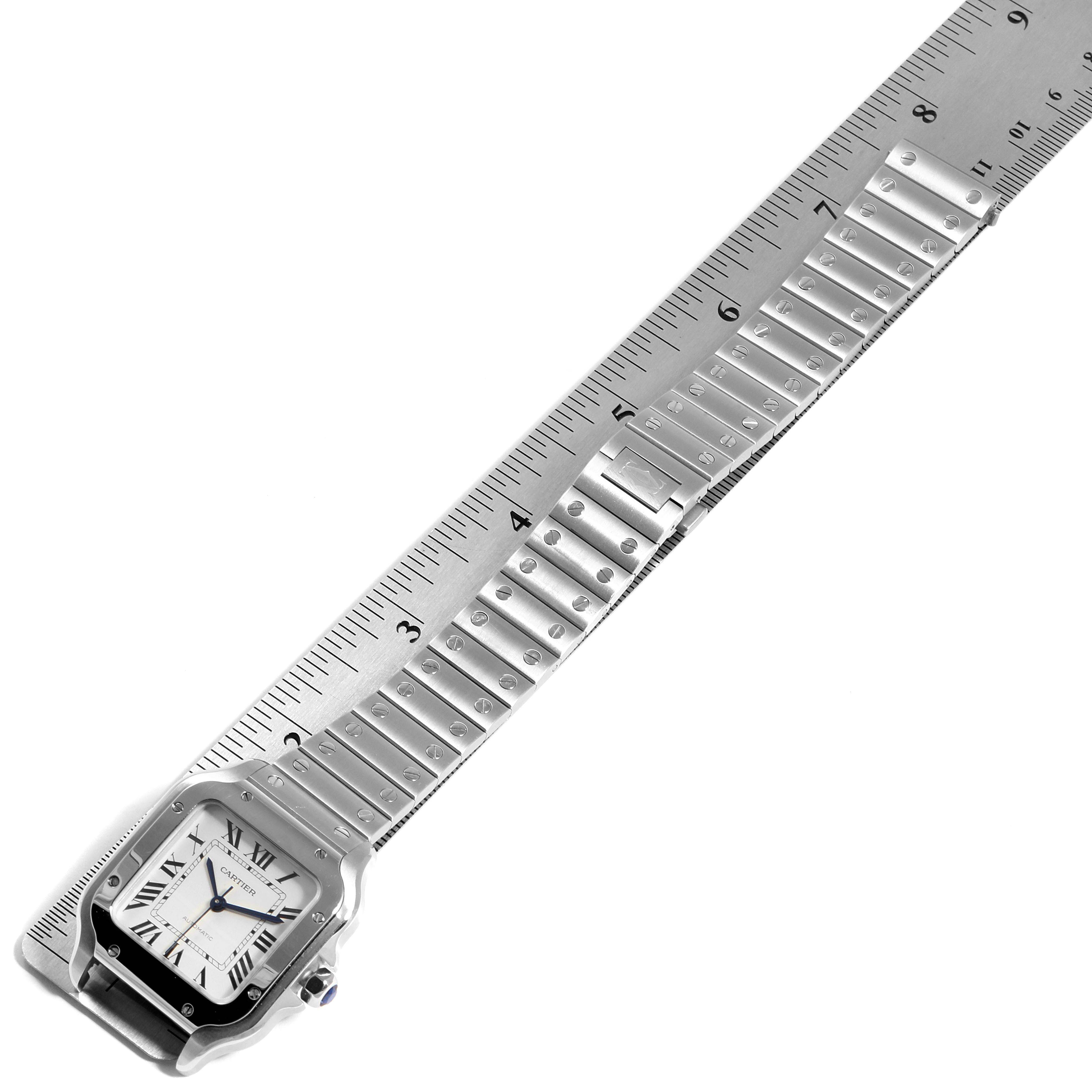 The Cartier Santos WSSA0010 Men's Stainless Steel Silver Dial WSSA0010 Men's Stainless Steel Silver Dial watch is shown from an overhead angle, with its face and bracelet laid out along a ruler.