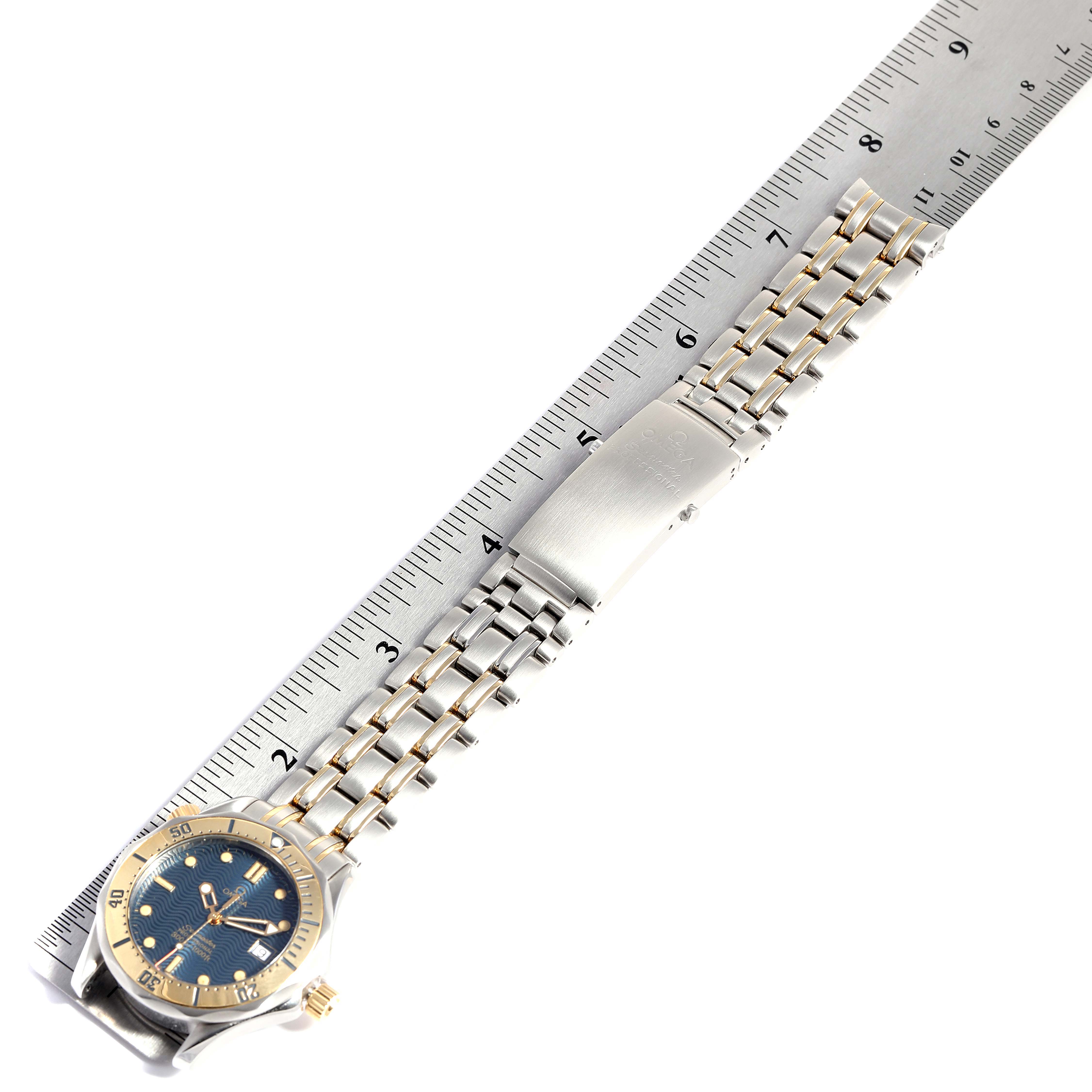 The Omega Seamaster 2342.80.00 Men's Steel and Gold (two tone) Blue Dial 2342.80.00 Men's Steel and Gold (two tone) Blue Dial watch is shown flat with the full bracelet and clasp visible next to a ruler for scale.
