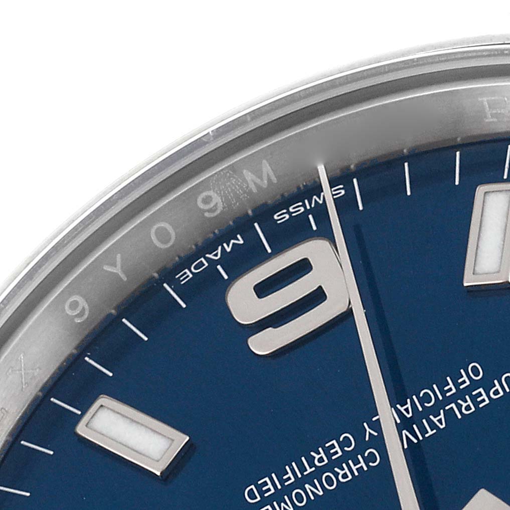 The close-up image shows a section of the dial and part of the bezel of a Rolex Oyster Perpetual 114200 Men's Stainless Steel Blue Dial 114200 Men's Stainless Steel Blue Dial watch, focusing on the 9 o'clock marker.