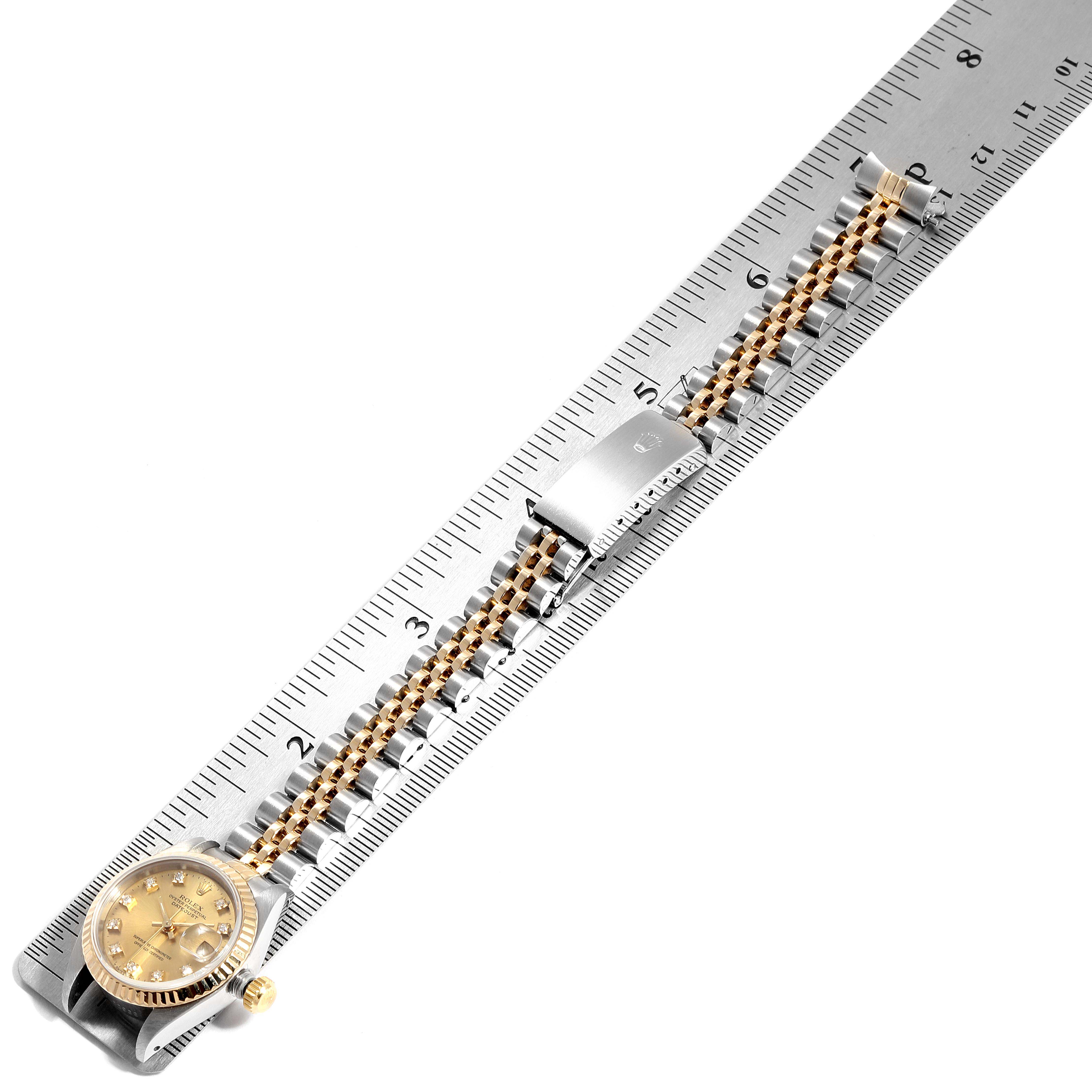 The image shows a Rolex Datejust 69173 Women
s Steel and Gold (two tone) Champagne Dial 69173 Women
s Steel and Gold (two tone) Champagne Dial watch laid flat next to a ruler, displaying its face and two-tone bracelet with clasp.