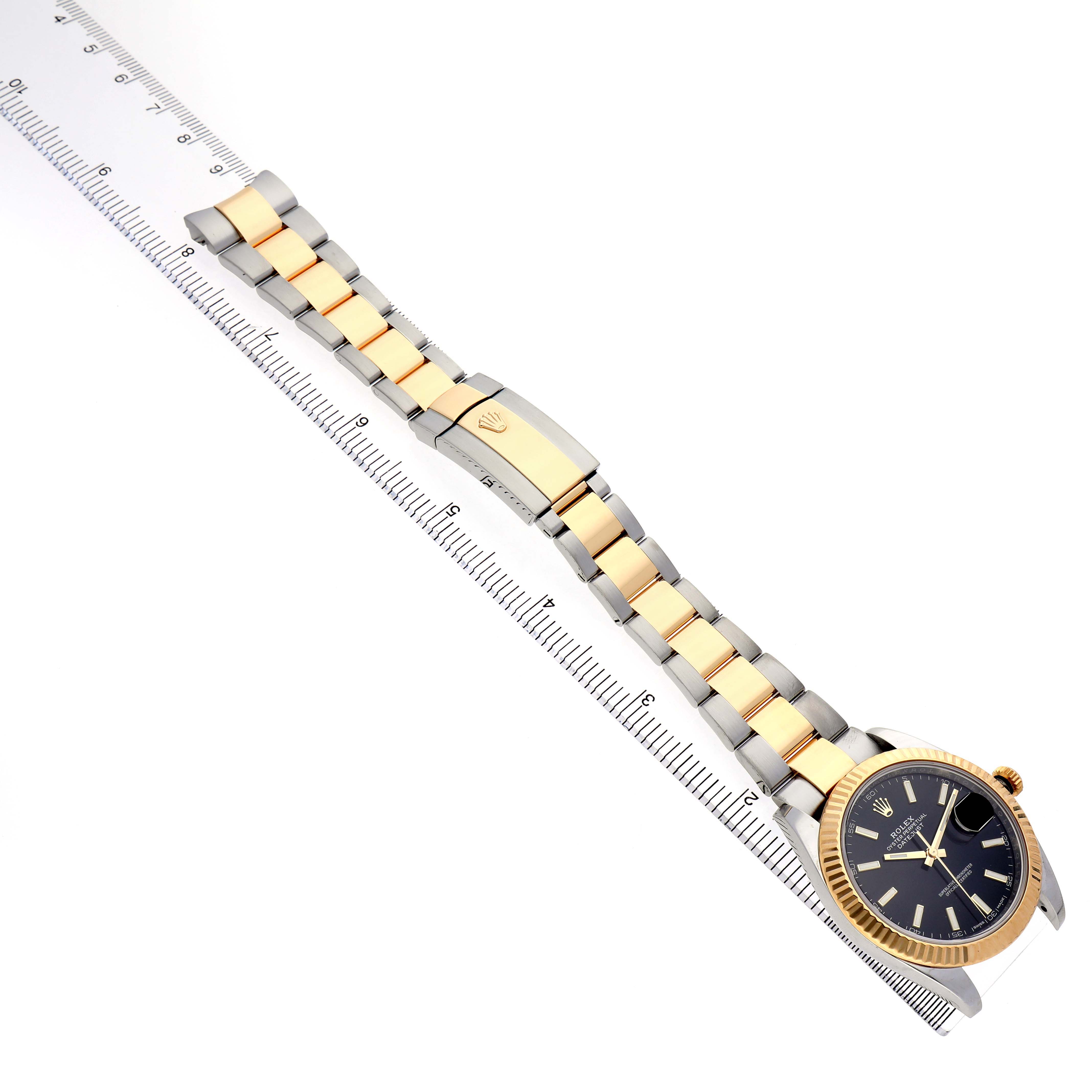 The image shows a top-down view of a Rolex Datejust 41 126333 Men's Steel and Gold (two tone) Black Dial, featuring its band and clasp on a ruler.