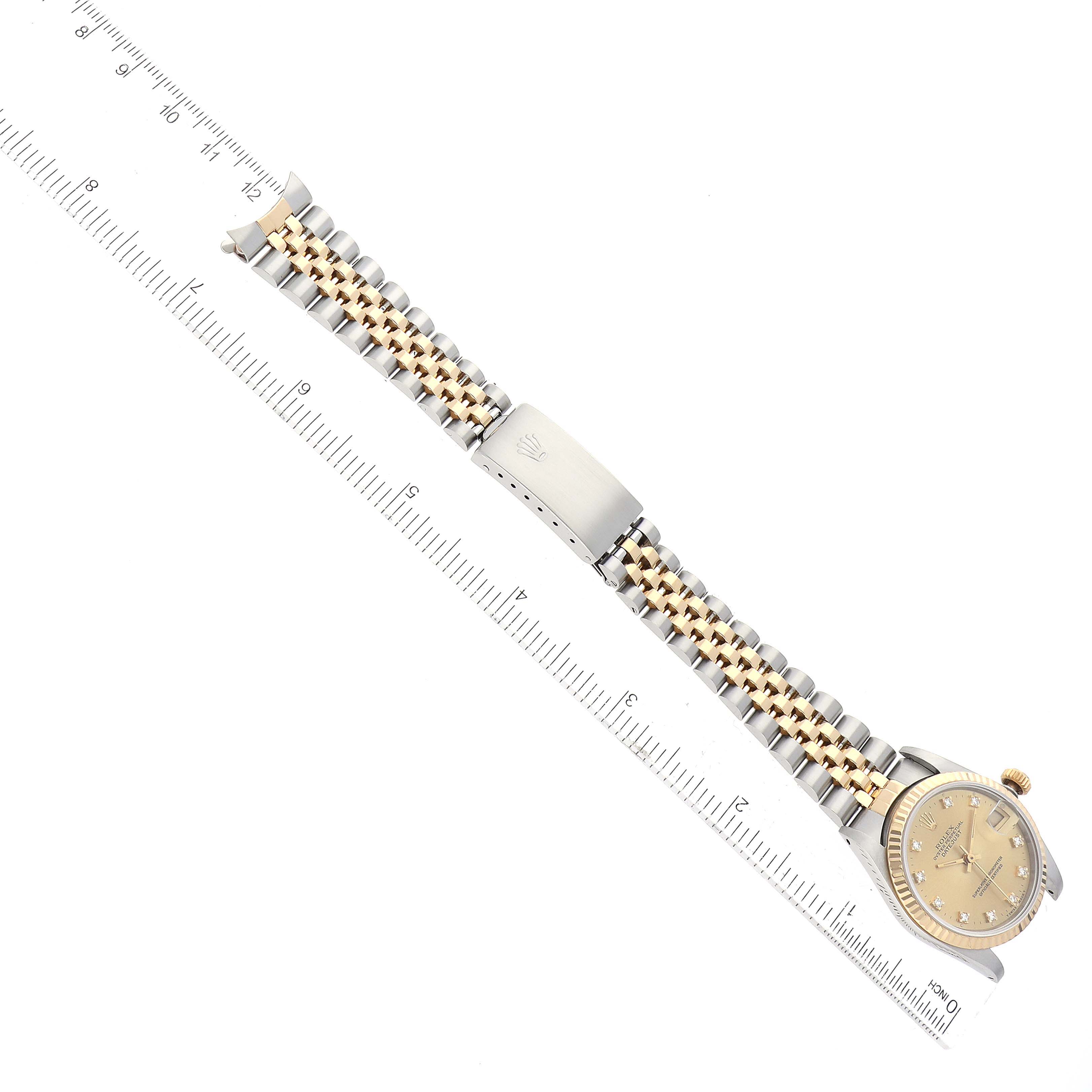 The image shows a mid-size Rolex watch laid flat with its bracelet fully extended, alongside a measuring ruler.
