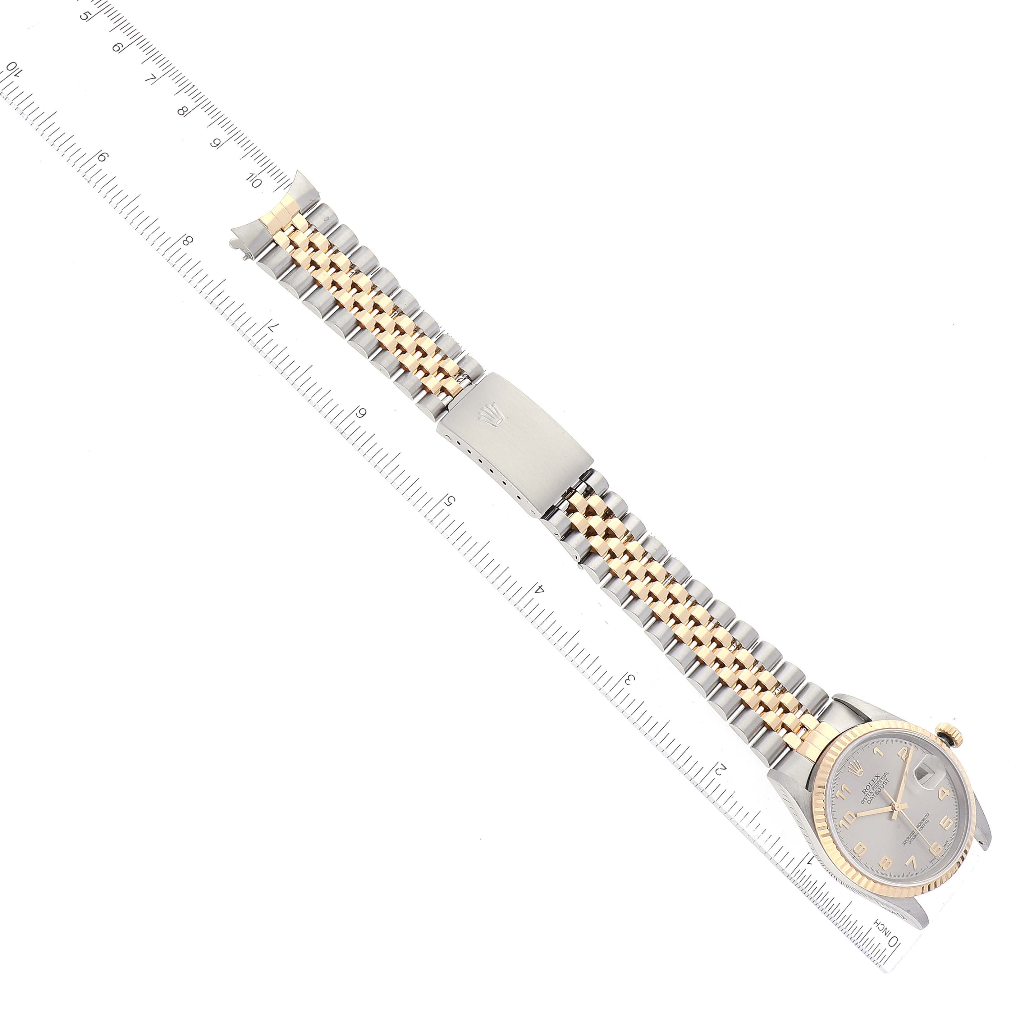 The Rolex Datejust 16233 Men's Steel and Gold (two tone) Grey Dial 16233 Men's Steel and Gold (two tone) Grey Dial watch is shown at a slightly angled top view, displaying its dial, crown, bracelet, and clasp against a measuring ruler.