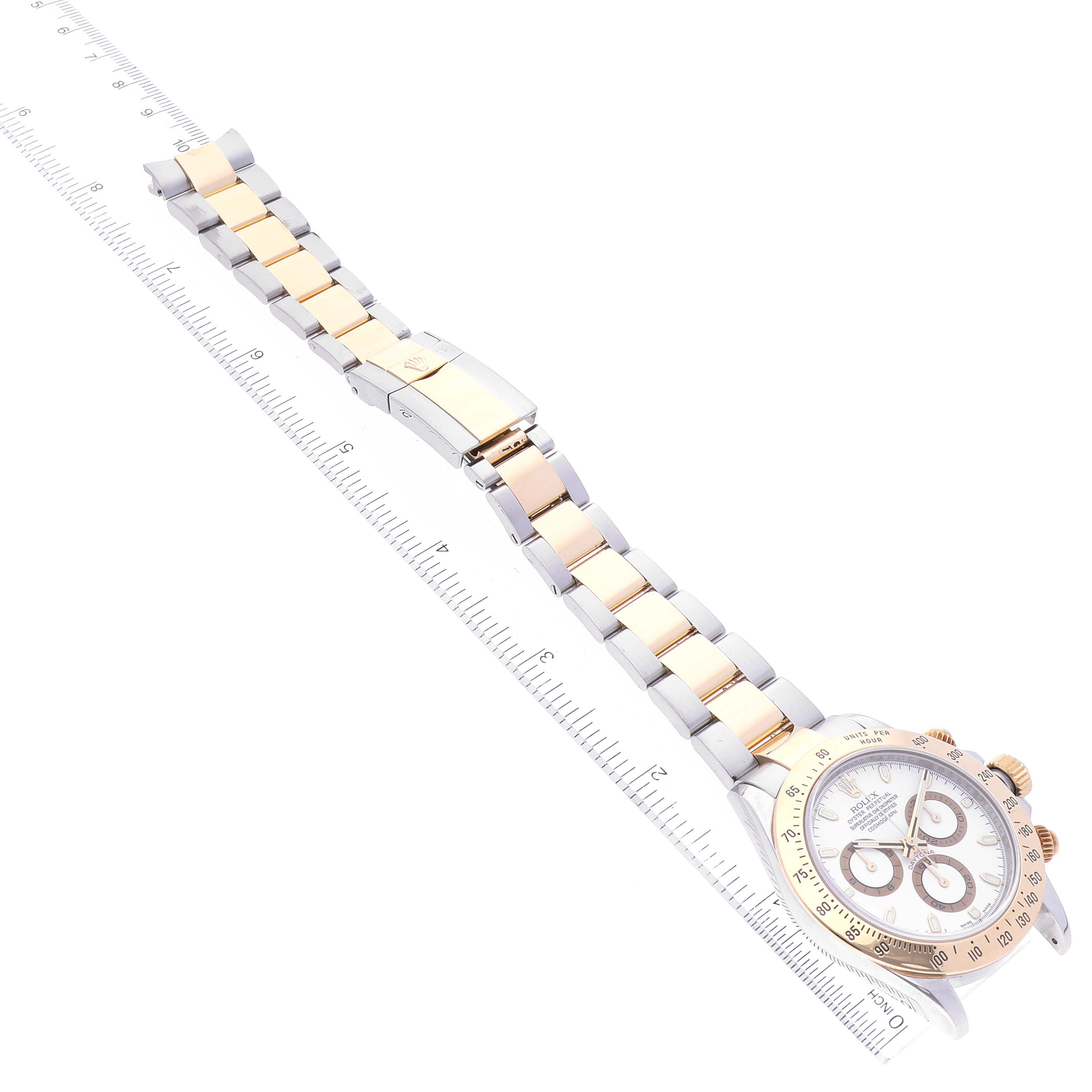 The image shows a top-down angle of a Rolex Daytona 116523 Men
s Steel and Gold (two tone) White Dial 116523 Men
s Steel and Gold (two tone) White Dial watch, displaying the full bracelet and the face of the watch alongside a ruler.