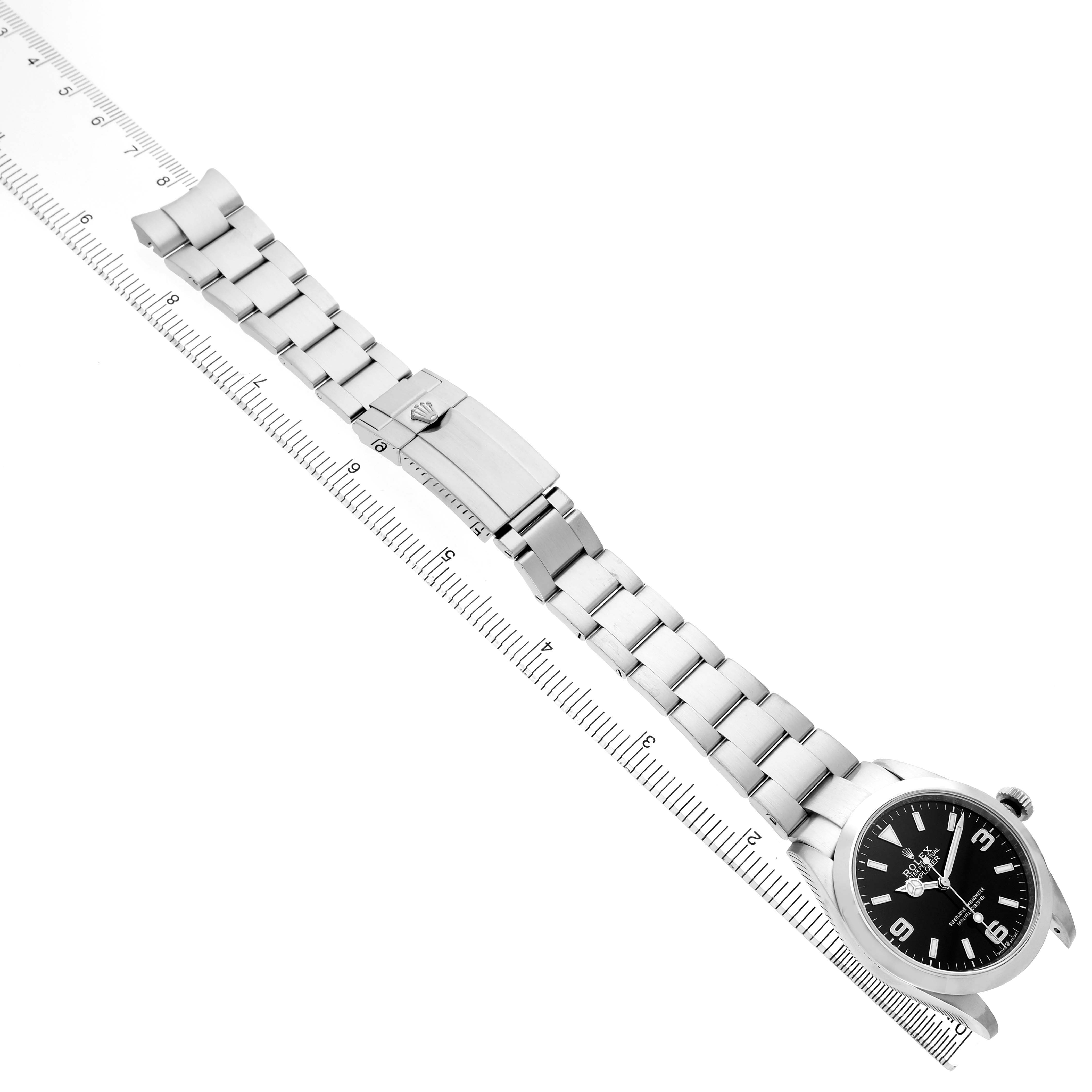 The Rolex Explorer 224270 Men's Stainless Steel Black Dial watch is shown from a top angle, featuring the face, clasp, and full bracelet laid out beside a ruler.
