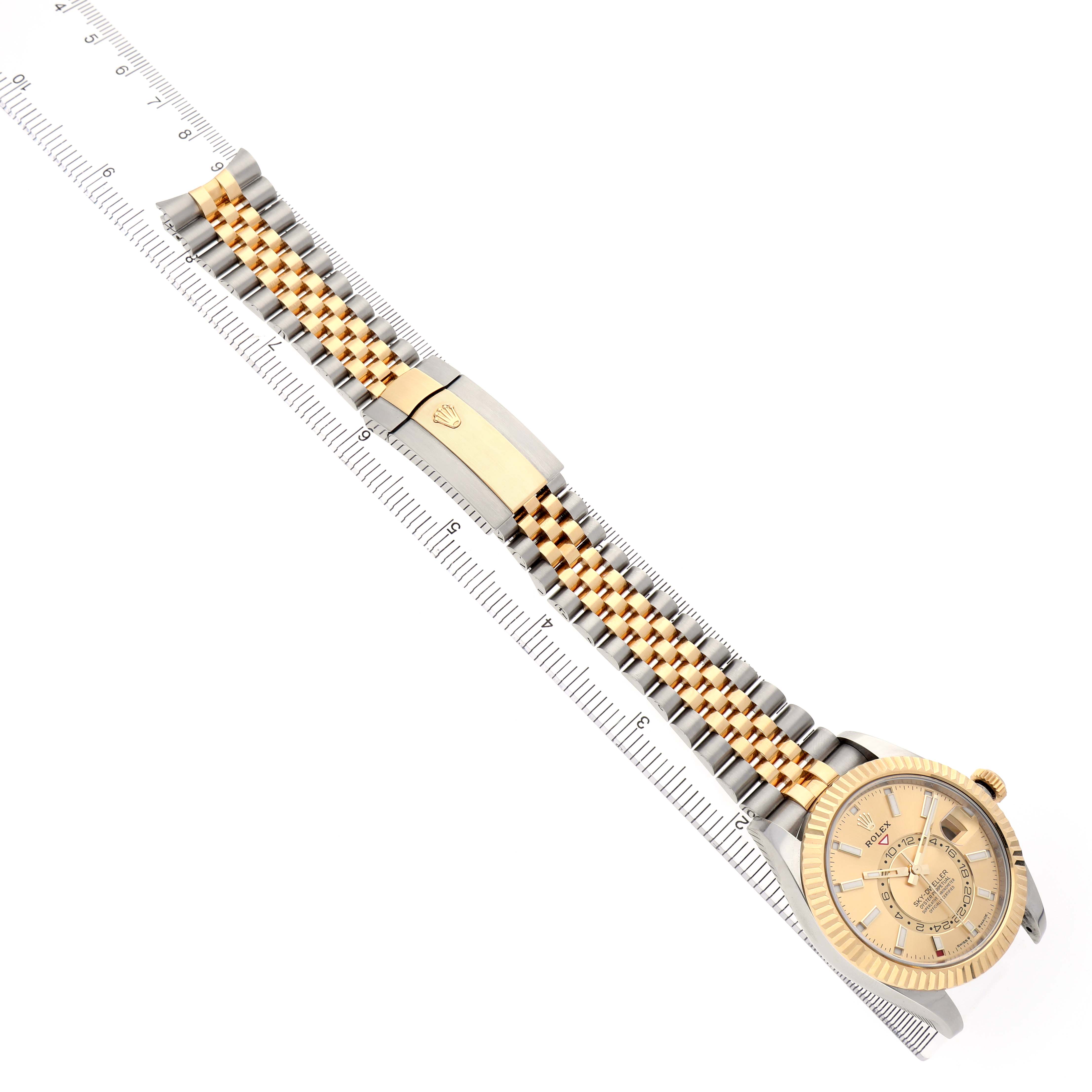 The Rolex Sky-Dweller 336933 Men's Steel and Gold (two tone) Champagne Dial watch is shown at a diagonal angle, highlighting the face, bezel, two-tone bracelet, and clasp alongside a ruler.