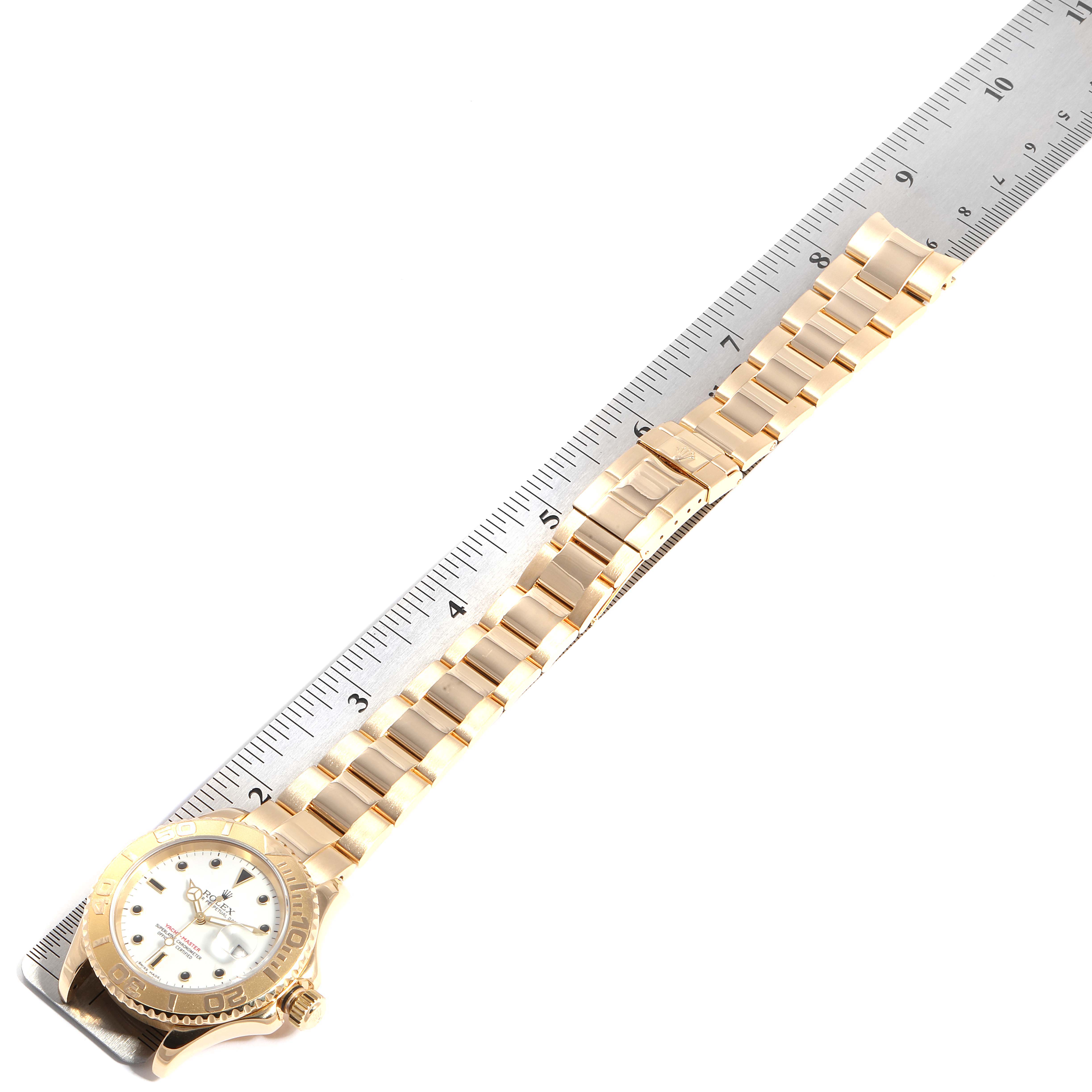 The image shows a Rolex Yacht-Master 16628 Men's Yellow Gold White Dial 16628 Men's Yellow Gold White Dial watch laid flat, next to a ruler, displaying its band and face.