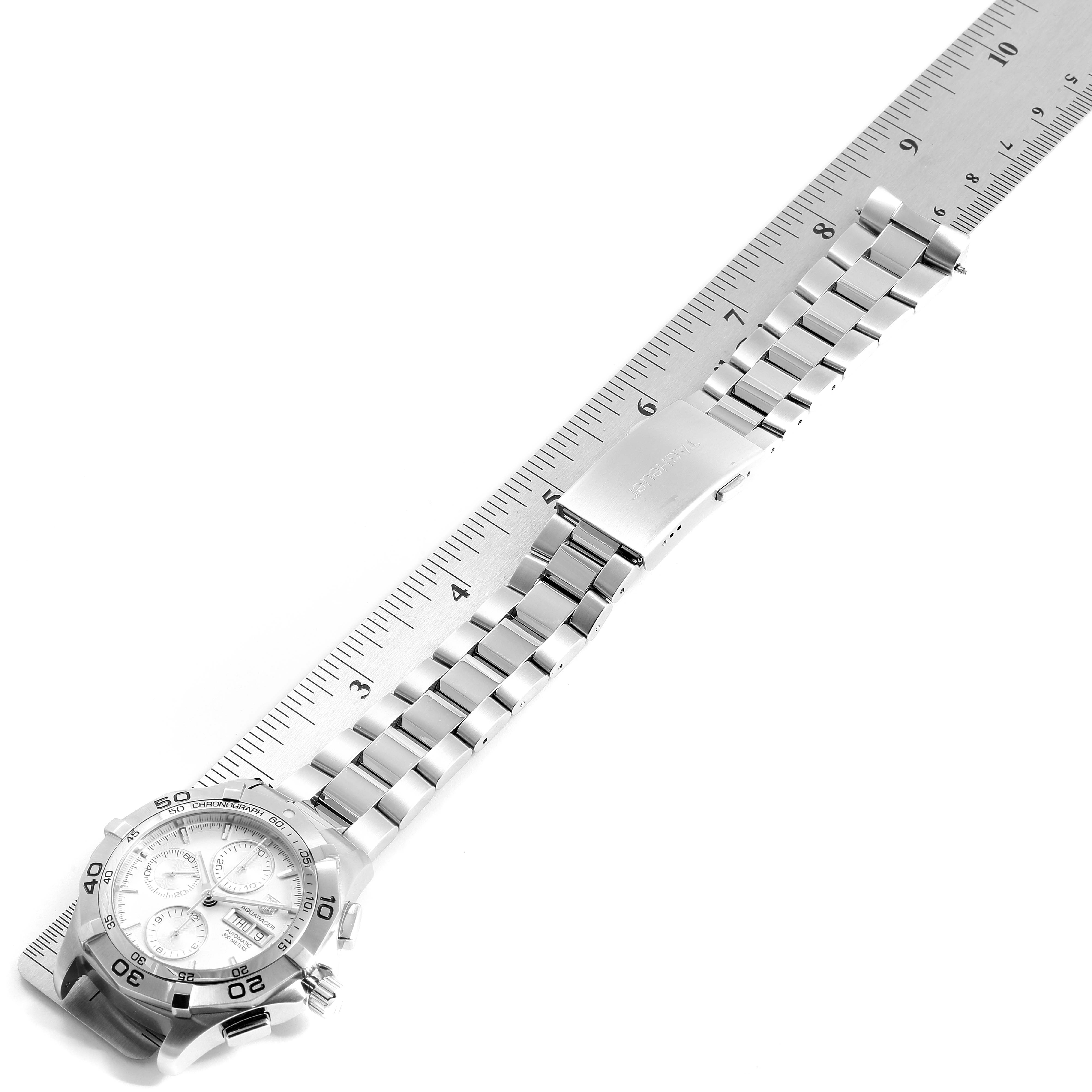 The image shows a top view of a Tag Heuer Aquaracer CAF2011.BA0815 Men's Stainless Steel Silver Dial CAF2011.BA0815 Men's Stainless Steel Silver Dial watch with its metal strap next to a ruler.