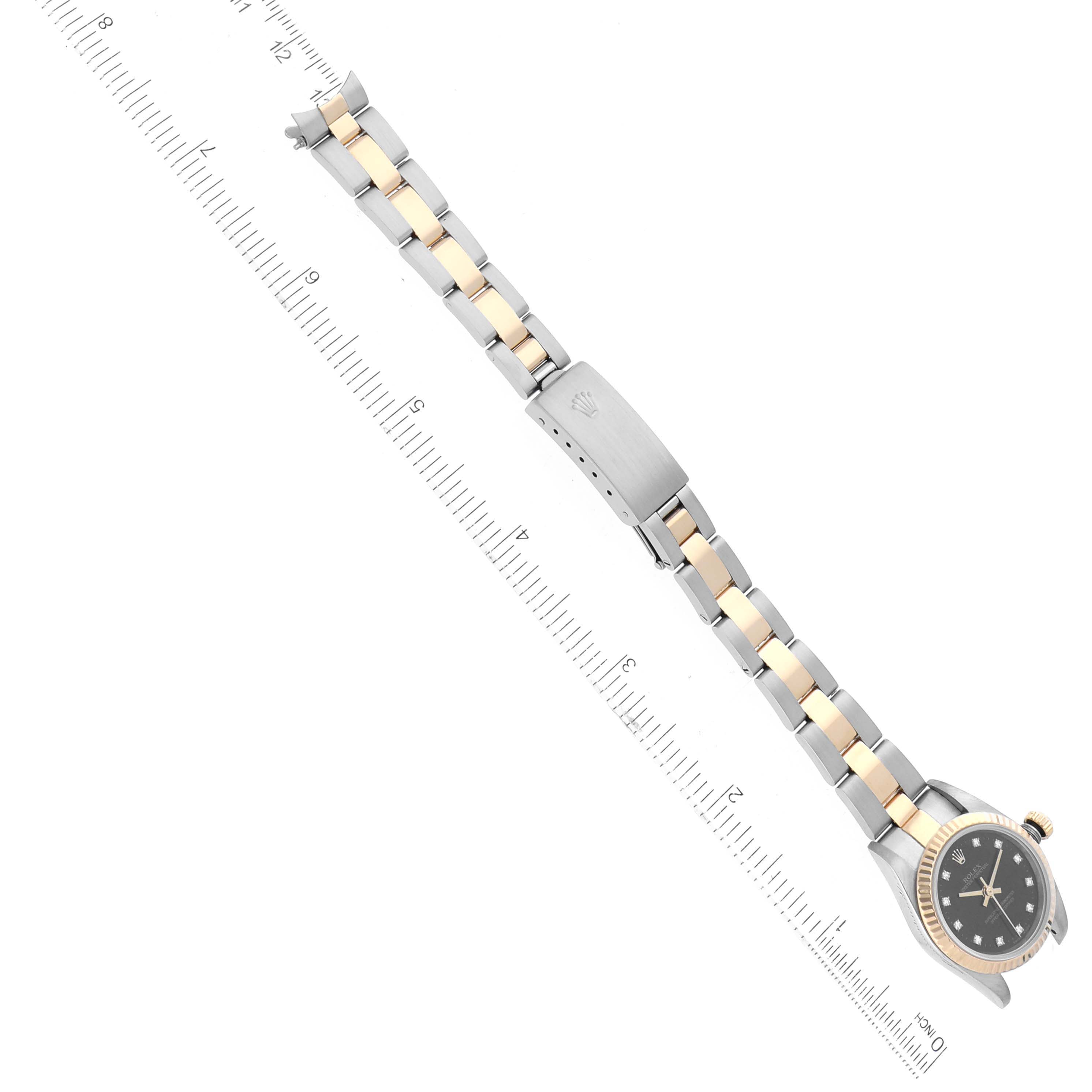 The Rolex Oyster Perpetual 76193 Women's Steel and Gold (two tone) Black Dial 76193 Women's Steel and Gold (two tone) Black Dial watch is shown from an angled top-down view, displaying its bracelet with a two-tone metal finish along with a ruler for scale.