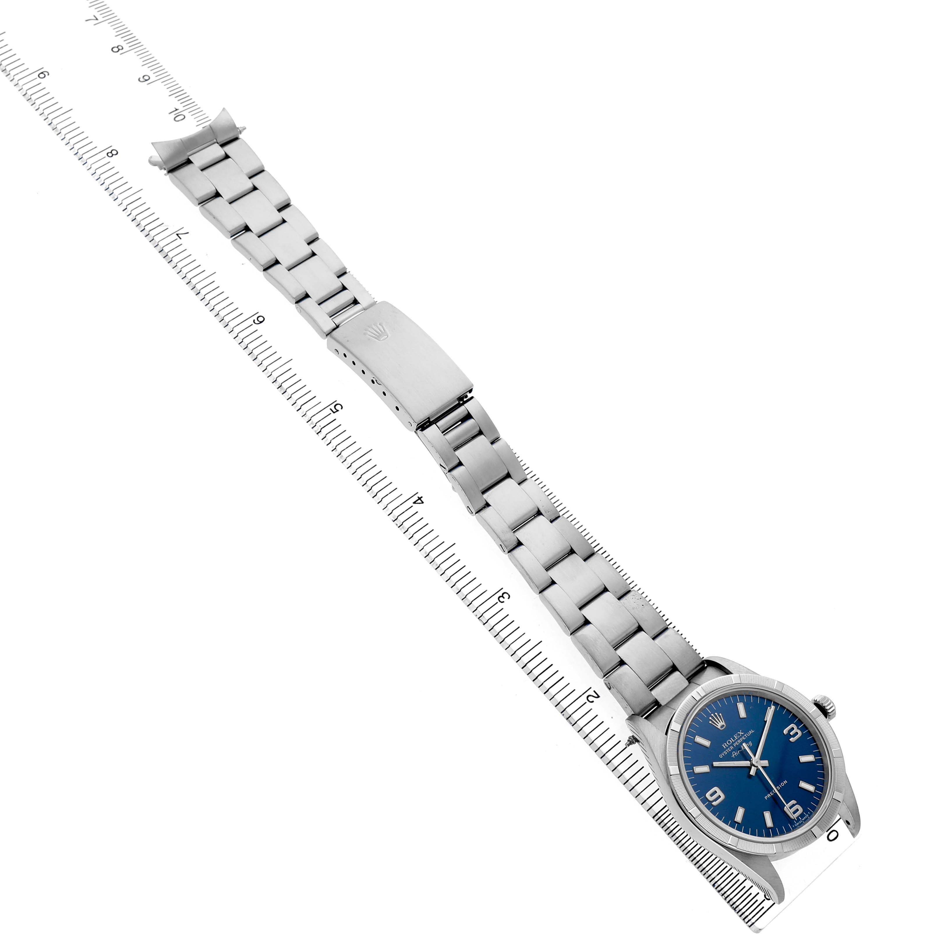 The Rolex Air-King 14010 Men's Stainless Steel Blue Dial watch is shown from a top-down angle, displaying its face, bracelet, and clasp alongside a ruler.