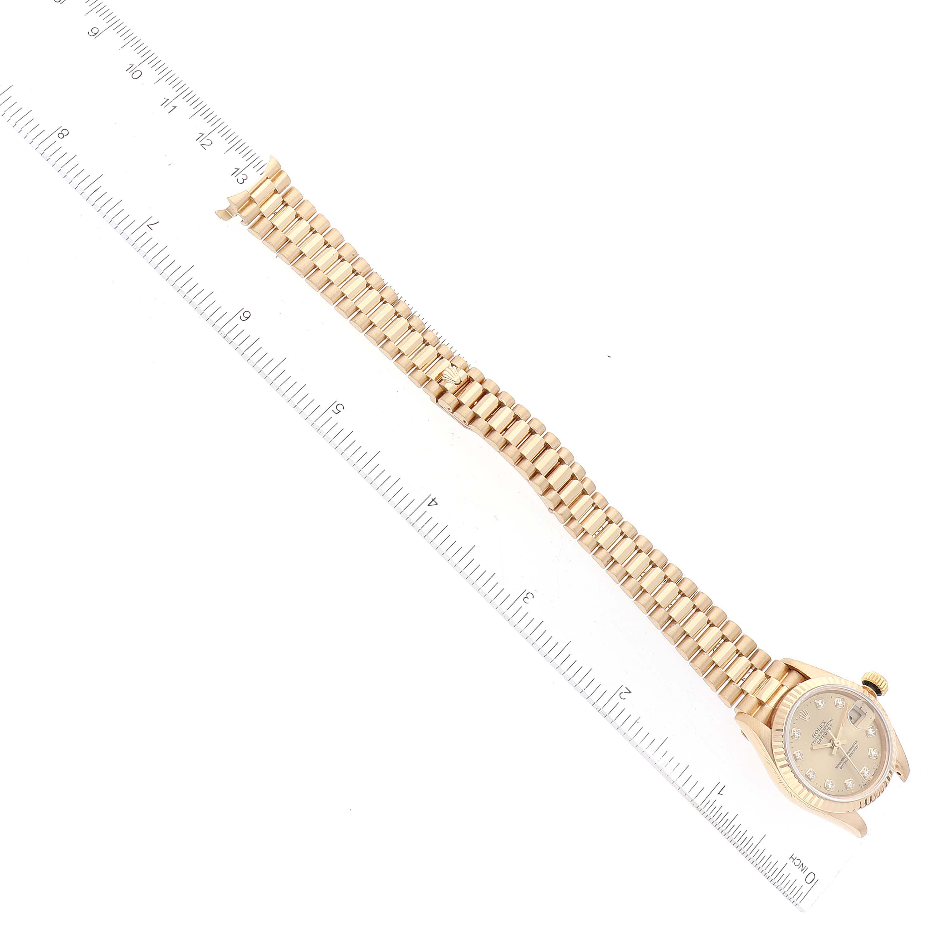 This image shows a Rolex President 69178 Women's Yellow Gold Champagne Dial 69178 Women's Yellow Gold Champagne Dial model watch laid flat with its band extended alongside a ruler.