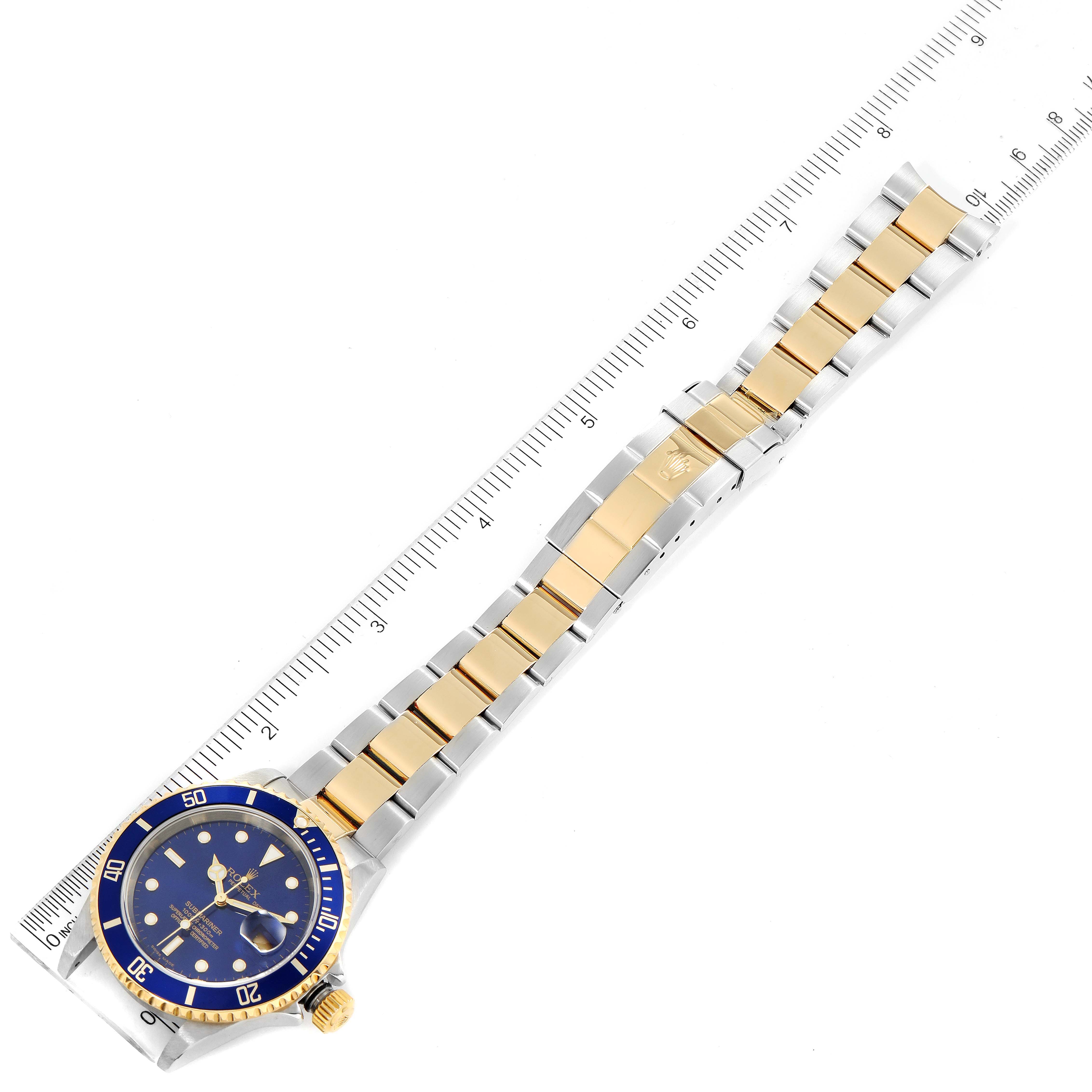 The image shows a Rolex Submariner 16613 Men's Steel and Gold (two tone) Blue Dial 16613 Men's Steel and Gold (two tone) Blue Dial watch at an overhead angle, displaying the dial, bezel, bracelet, clasp, and a ruler for scale.