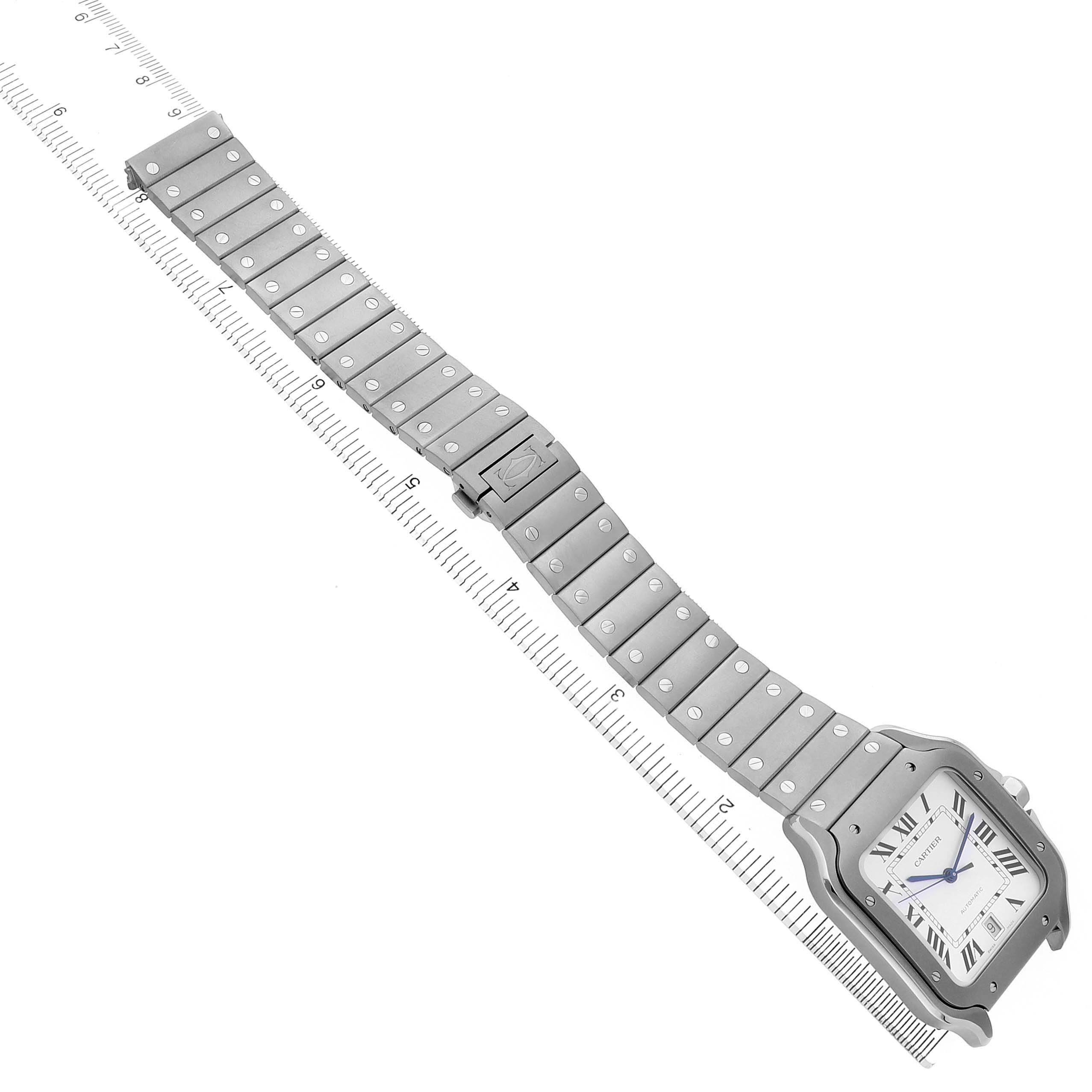 The Cartier Santos WSSA0089 Men's Titanium Silver Dial watch is shown diagonally with a full view of its face and metal bracelet against a measuring scale.