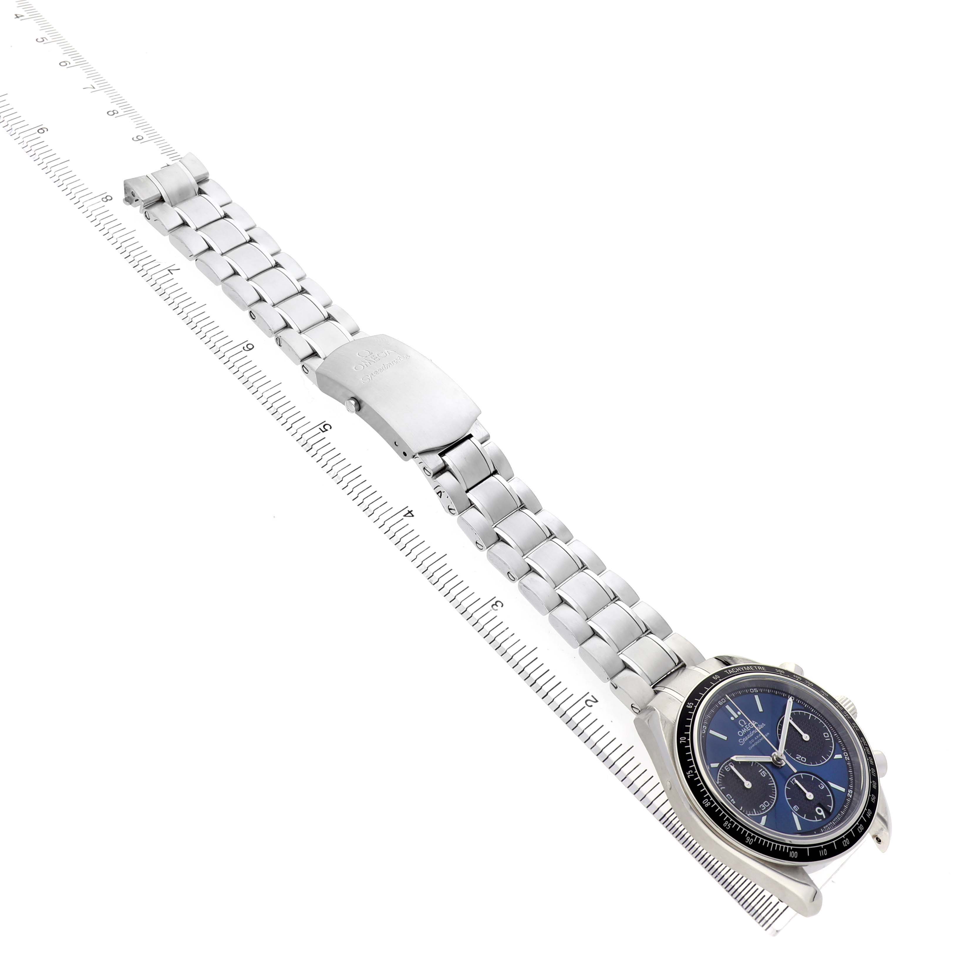 The Omega Speedmaster 326.30.40.50.03.001 Men's Stainless Steel Blue Dial watch is shown at a tilted angle, highlighting its dial, bezel, and metal bracelet alongside a ruler.