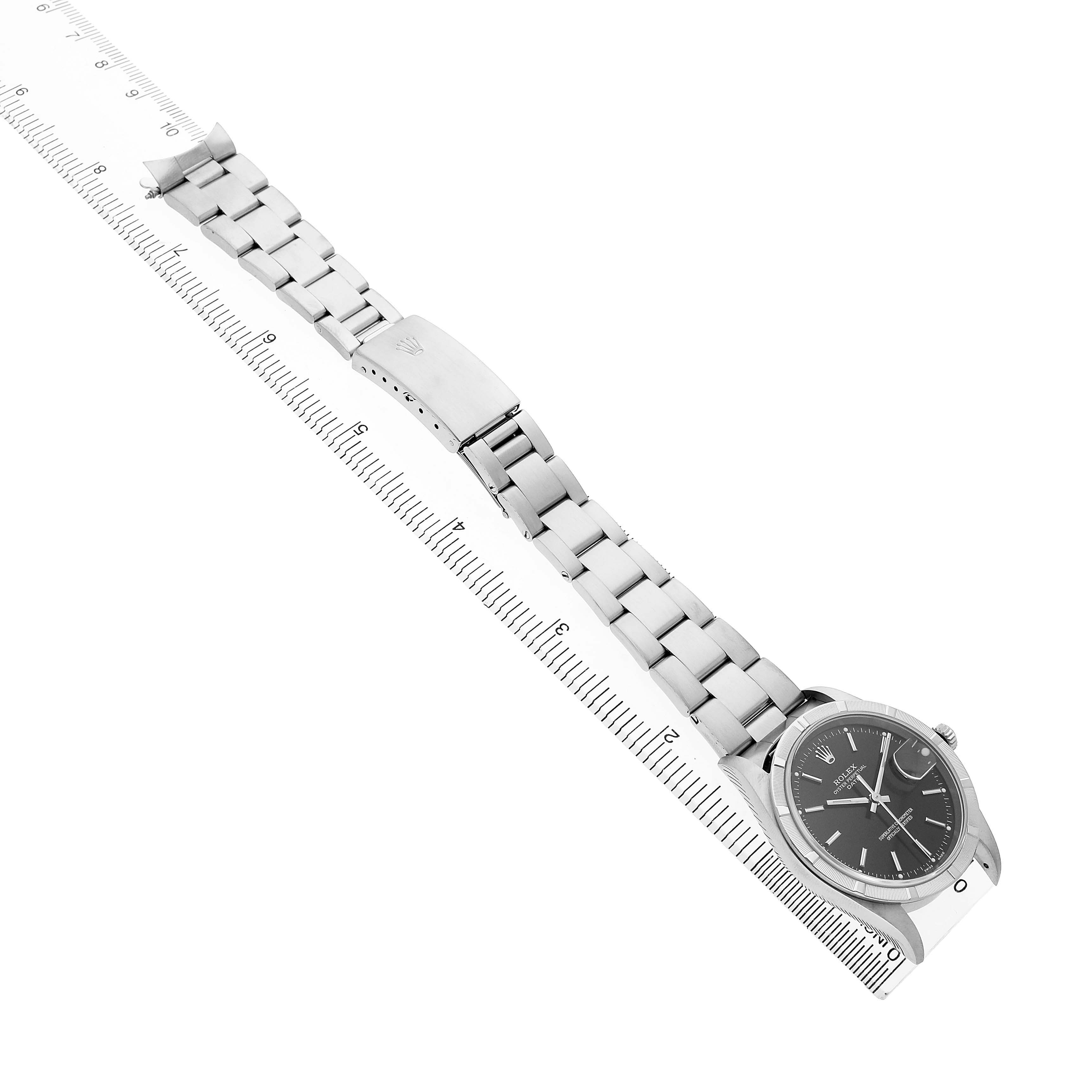 The Rolex Date 15210 Men's Stainless Steel Black Dial watch is shown at an angle highlighting the full length of the bracelet and clasp, alongside a ruler for scale.