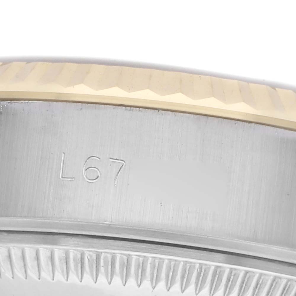The image shows a close-up of the side of a Rolex Datejust 69173 Women
s Steel and Gold (two tone) White Dial 69173 Women
s Steel and Gold (two tone) White Dial, focusing on the fluted bezel and part of the case with an engraving.