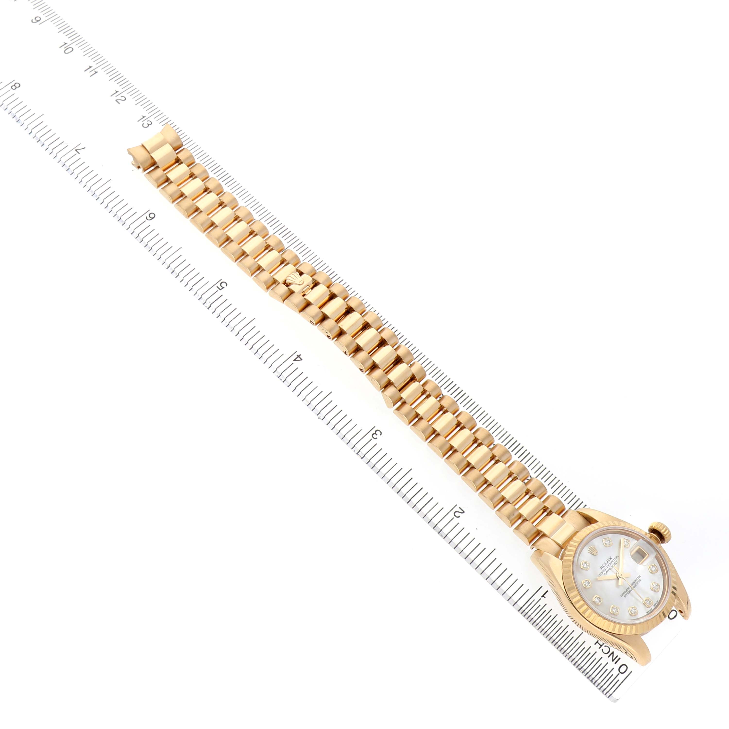The Rolex President 179178 Women's Yellow Gold Mother of Pearl Dial model watch is shown at an angle displaying its gold bracelet and dial placed against a ruler.