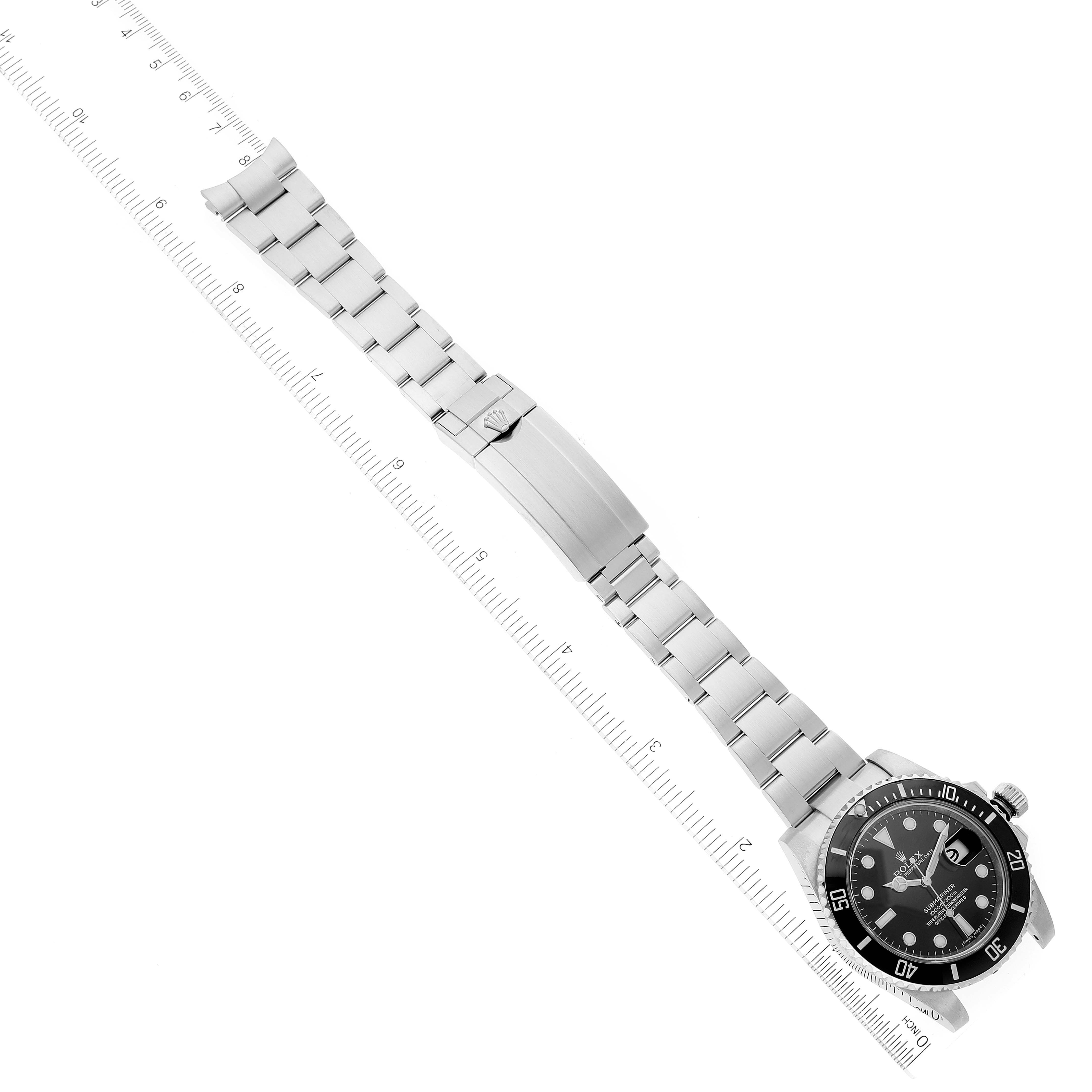 The Rolex Submariner 116610 Men
s Stainless Steel Black Dial 116610 Men
s Stainless Steel Black Dial watch is shown in a top-down angle, displaying its dial, bezel, and bracelet with a ruler beside it for scale.