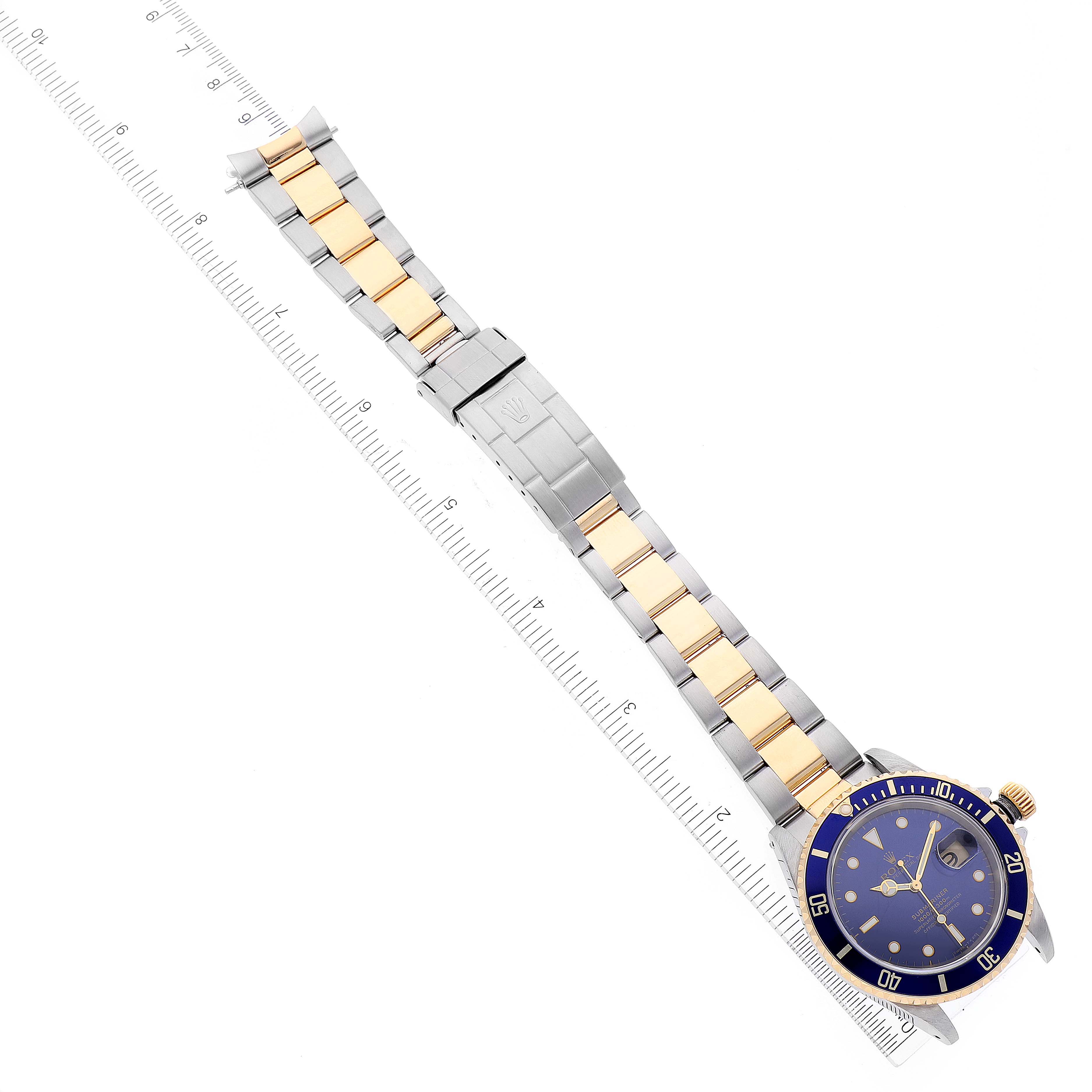 The image shows a top-down view of a Rolex Submariner 16613 Men's Steel and Gold (two tone) Blue Dial 16613 Men's Steel and Gold (two tone) Blue Dial watch, featuring the dial, bezel, and full bracelet placed against a ruler.