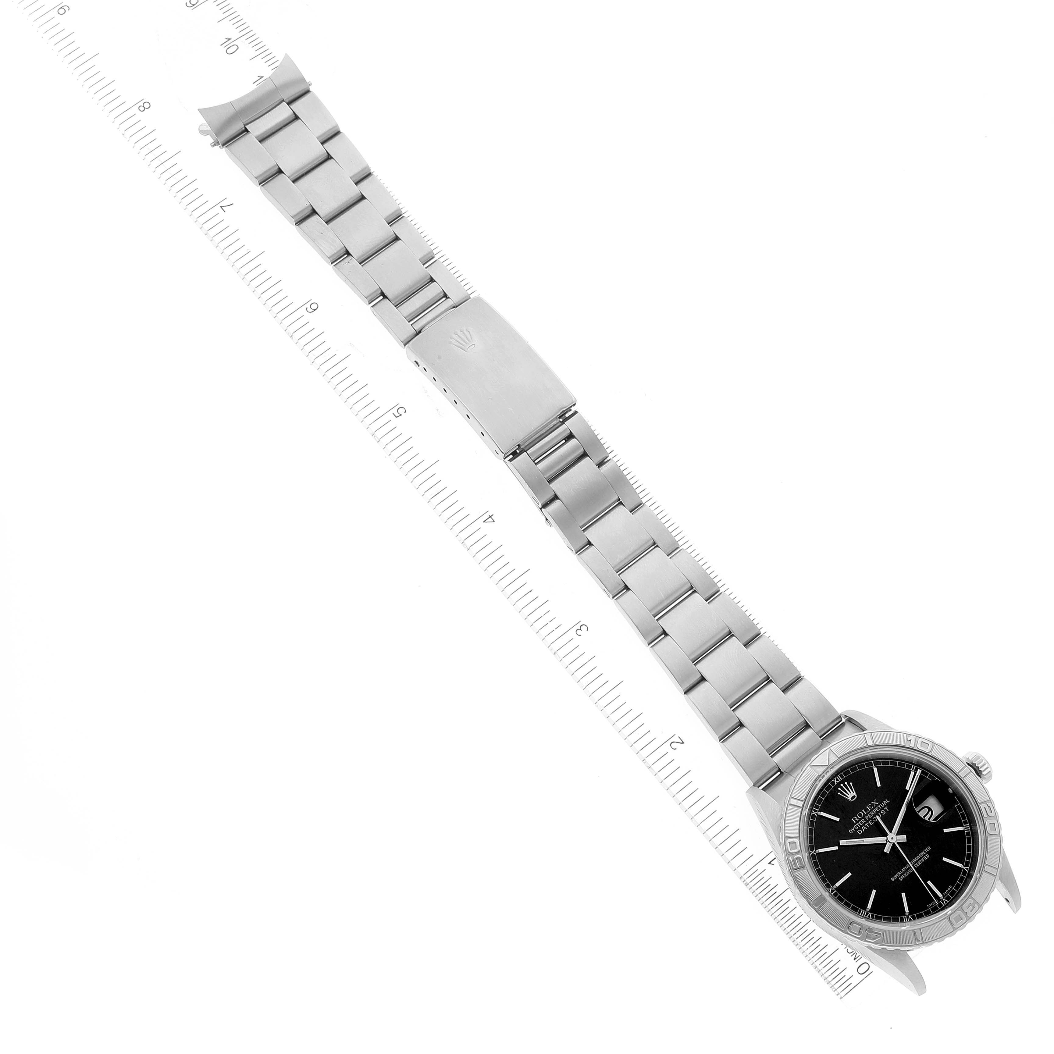 The Rolex Turn-o-Graph 16264 Men
s Stainless Steel Black Dial 16264 Men
s Stainless Steel Black Dial watch is shown laying flat with a full view of the face, bezel, and bracelet, extended alongside a ruler.