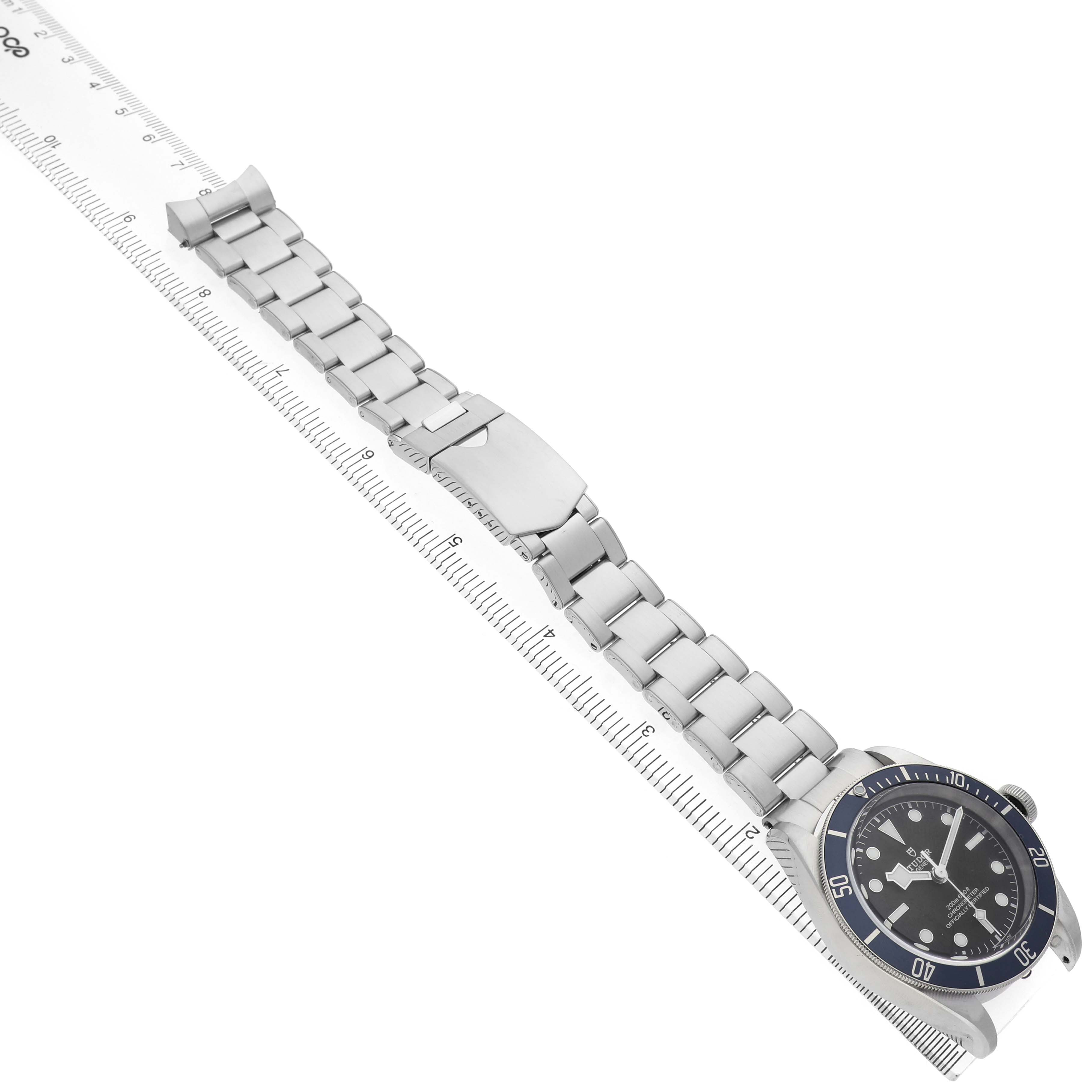 The Tudor Heritage Black Bay 79230B Men's Stainless Steel Black Dial watch is shown at an angle highlighting the face, bezel, bracelet, and clasp.