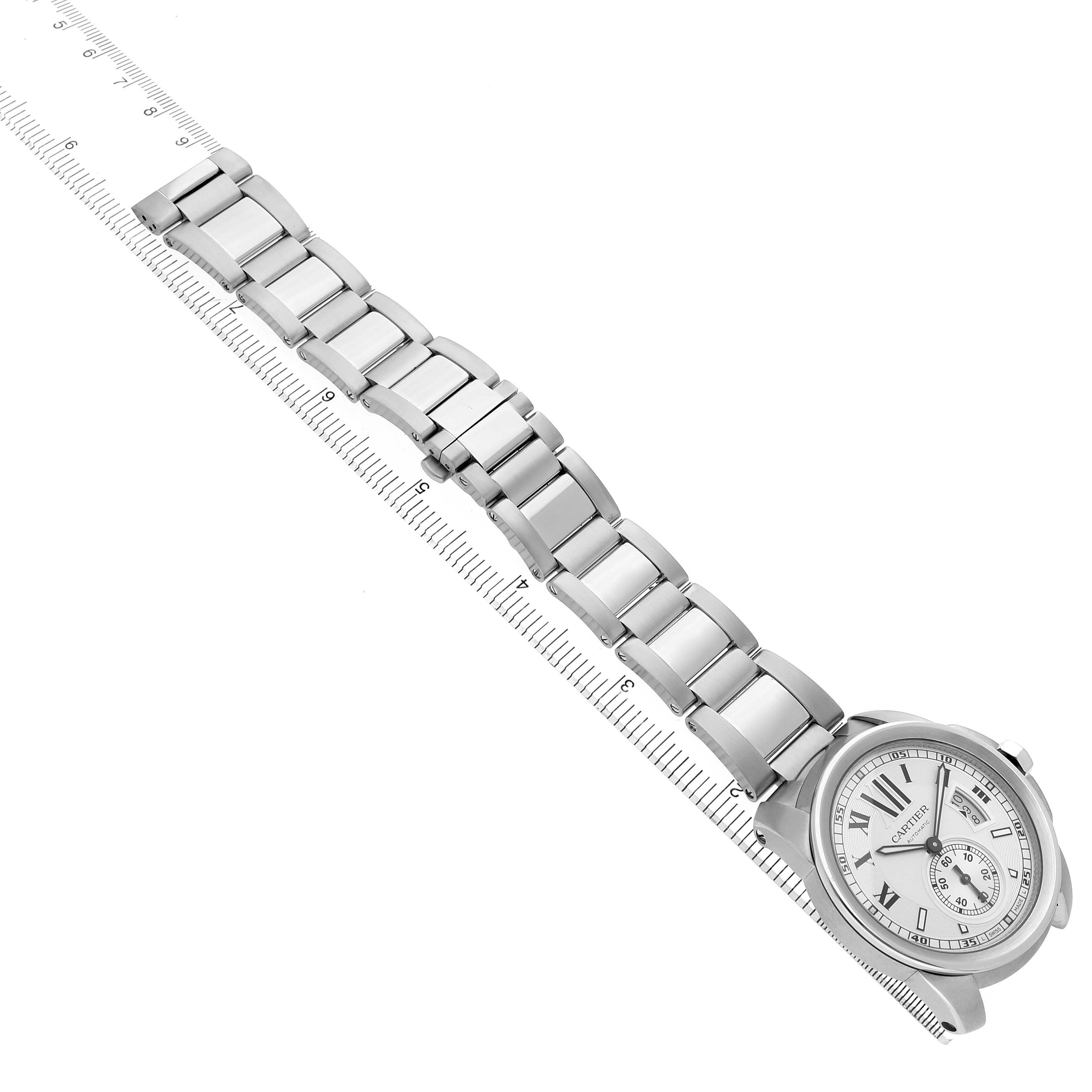 The Calibre de Cartier watch is shown from an overhead angle, highlighting its face and metal bracelet lying along a ruler.