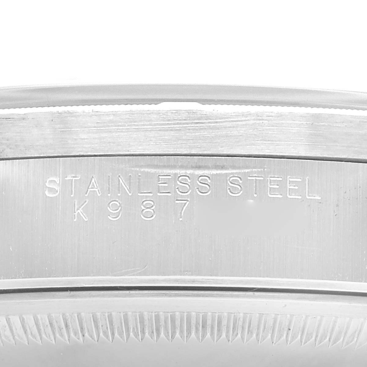 This image shows a close-up of the side of the case of a Rolex Date 15210 Men's Stainless Steel Blue Dial 15210 Men's Stainless Steel Blue Dial model watch, engraved with "STAINLESS STEEL K 987."