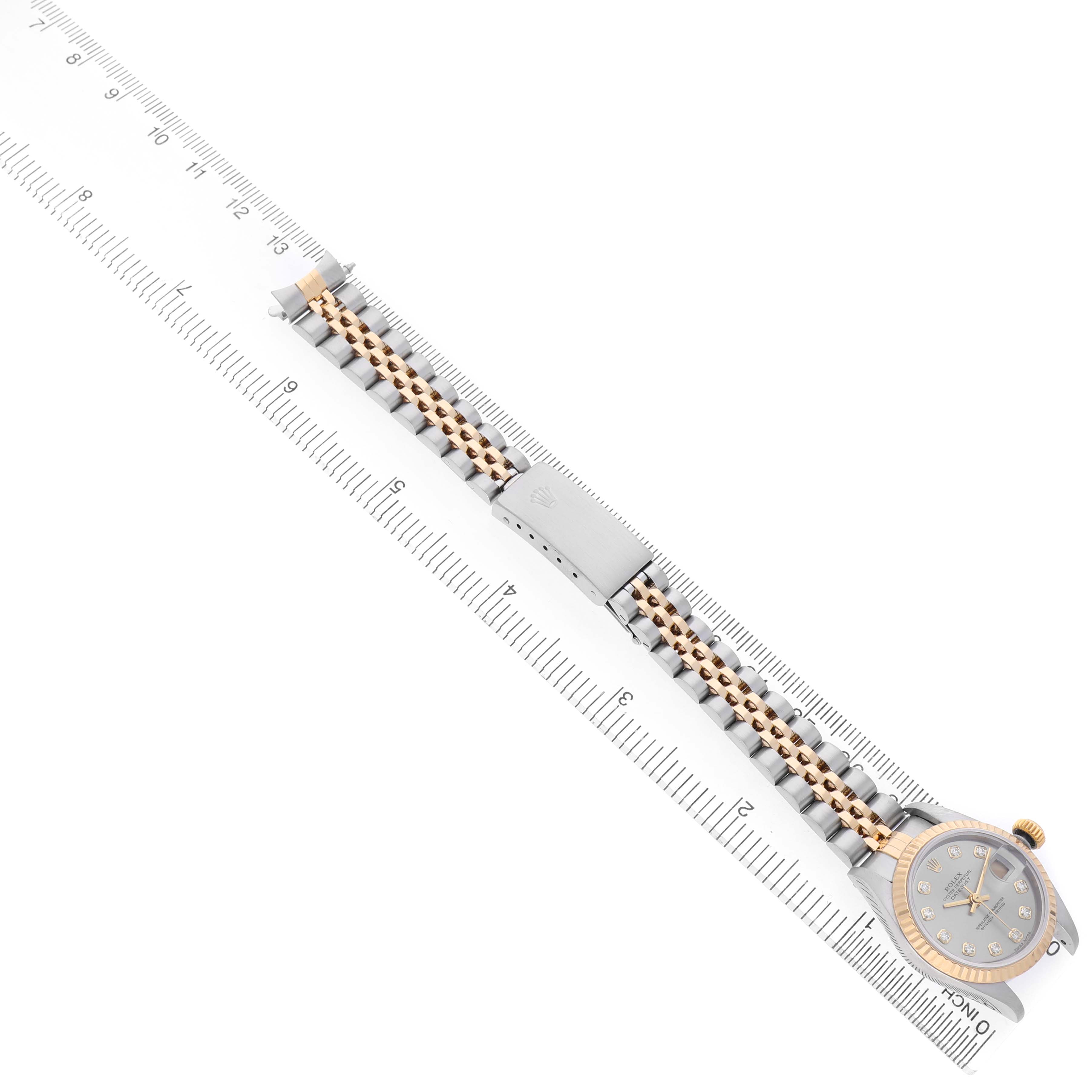 The Rolex Datejust 79173 Women's Steel and Gold (two tone) Silver Dial watch is shown from a top view, featuring the entire bracelet and case alongside a ruler for scale.