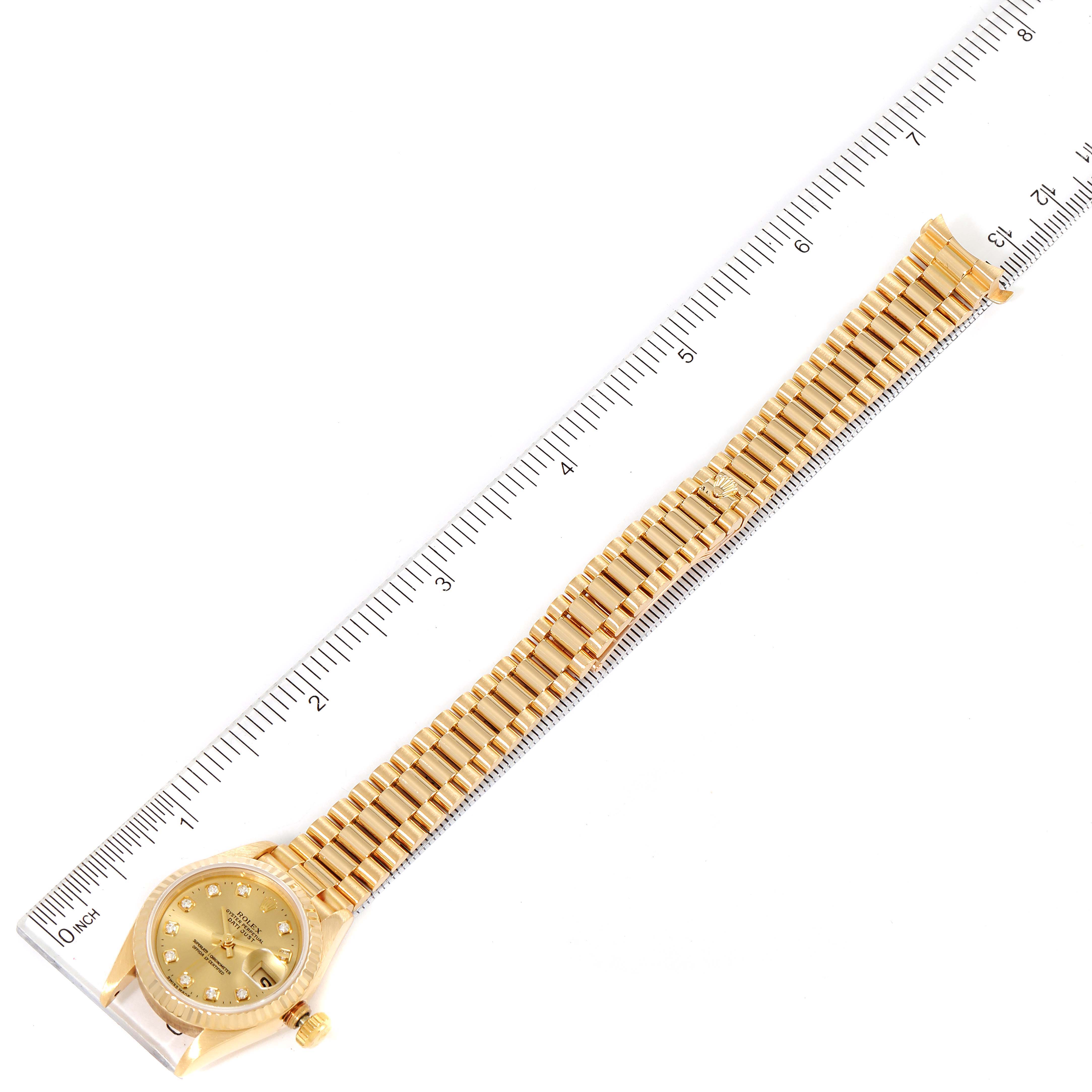 This image shows a Rolex President 69178 Women
s Yellow Gold Champagne Dial 69178 Women
s Yellow Gold Champagne Dial model watch laid flat next to a ruler, displaying its dial, bezel, and bracelet.