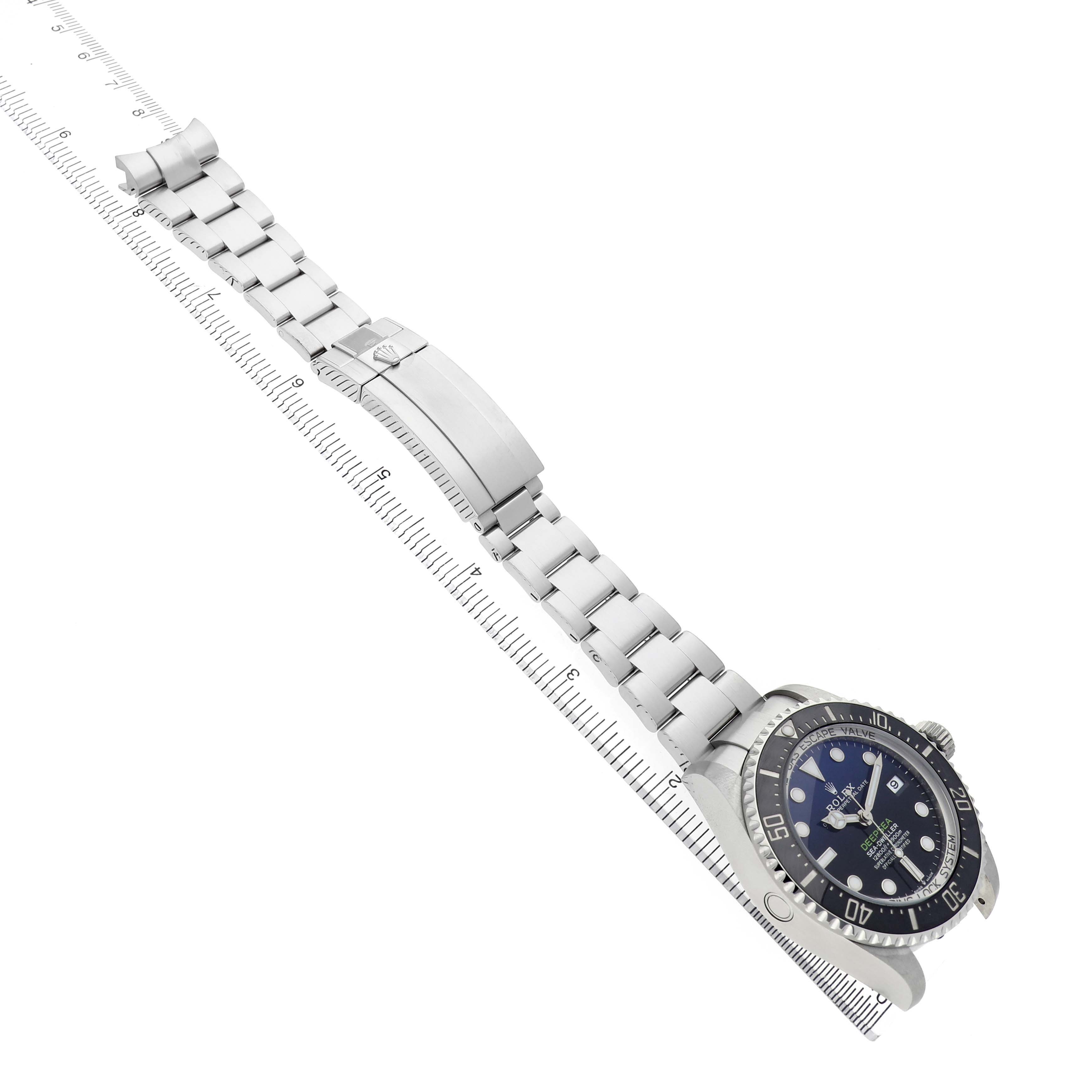 The Rolex Sea-Dweller 126660 Men's Stainless Steel Blue Dial watch is angled diagonally with a visible dial, bezel, bracelet, and clasp alongside a ruler.
