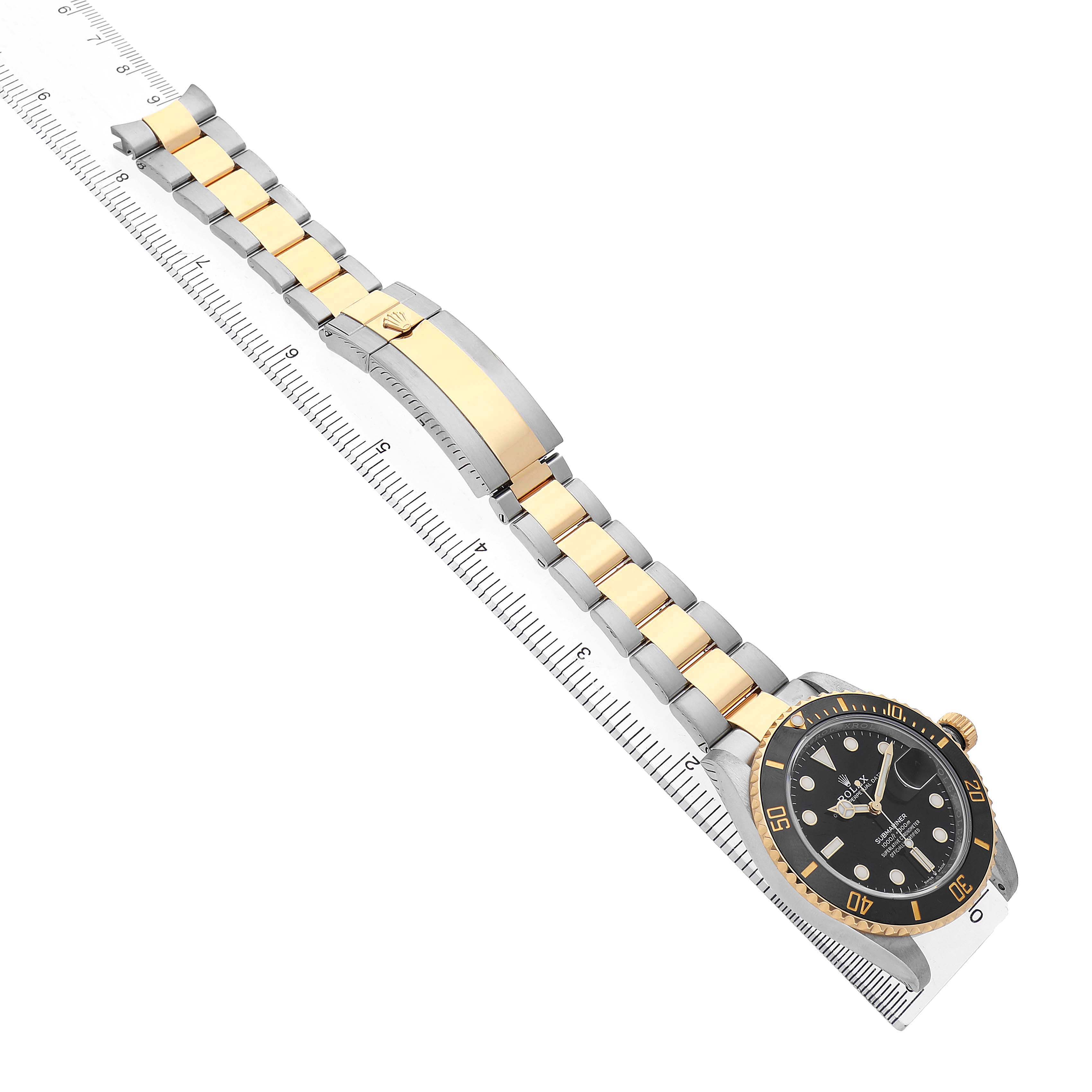 The Rolex Submariner M126613LN-0002 Men's Steel and Gold (two tone) Black Dial watch is shown at an angle, displaying its two-tone bracelet and watch face against a measuring scale.