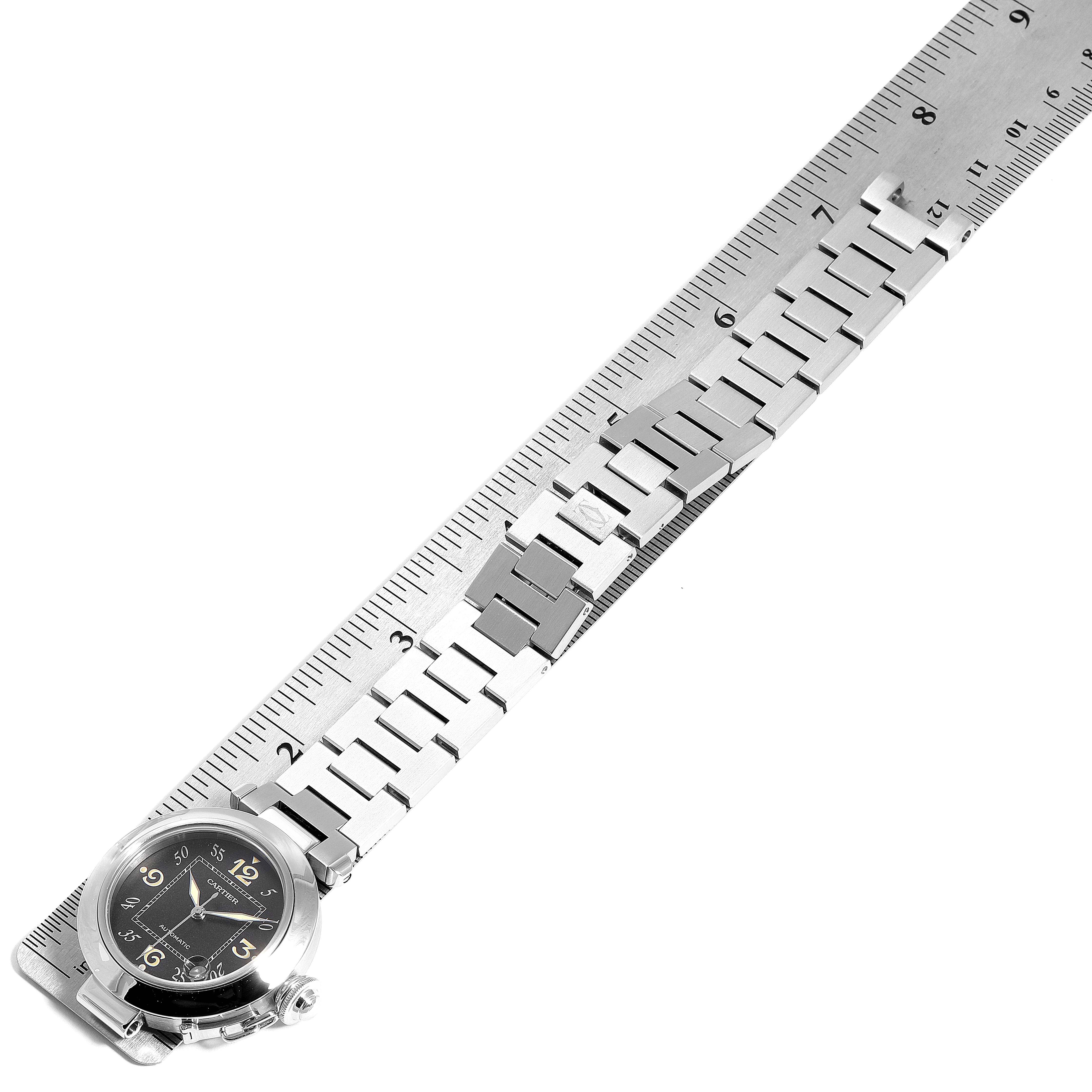 The image shows the Cartier Pasha W31043M7 Men's Stainless Steel Black Dial W31043M7 Men's Stainless Steel Black Dial watch placed against a ruler, showcasing its face, bracelet, and clasp.