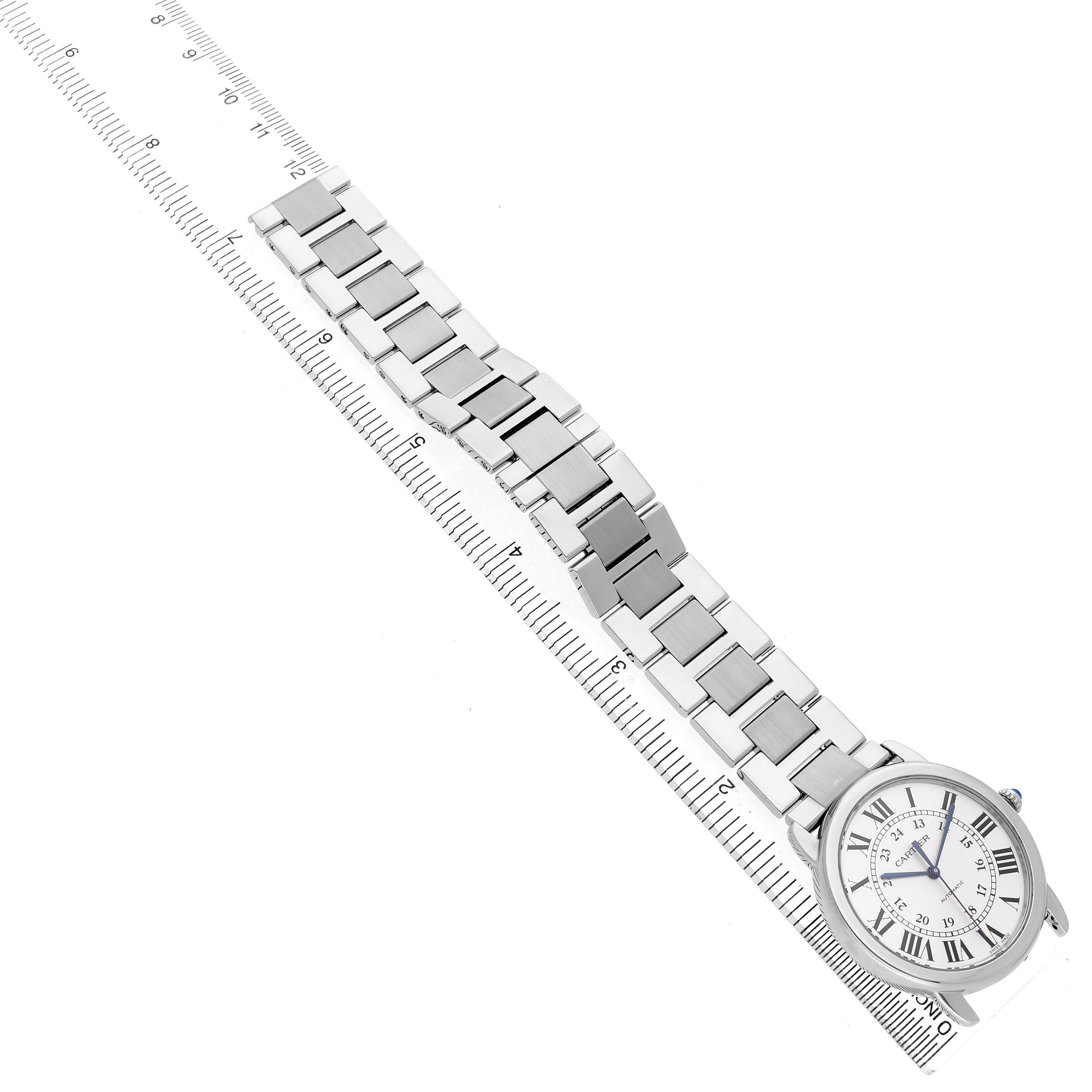 The Cartier Ronde WSRN0012 Men's Stainless Steel Silver Dial watch is shown from above, displaying its face, bracelet, and part of a ruler.