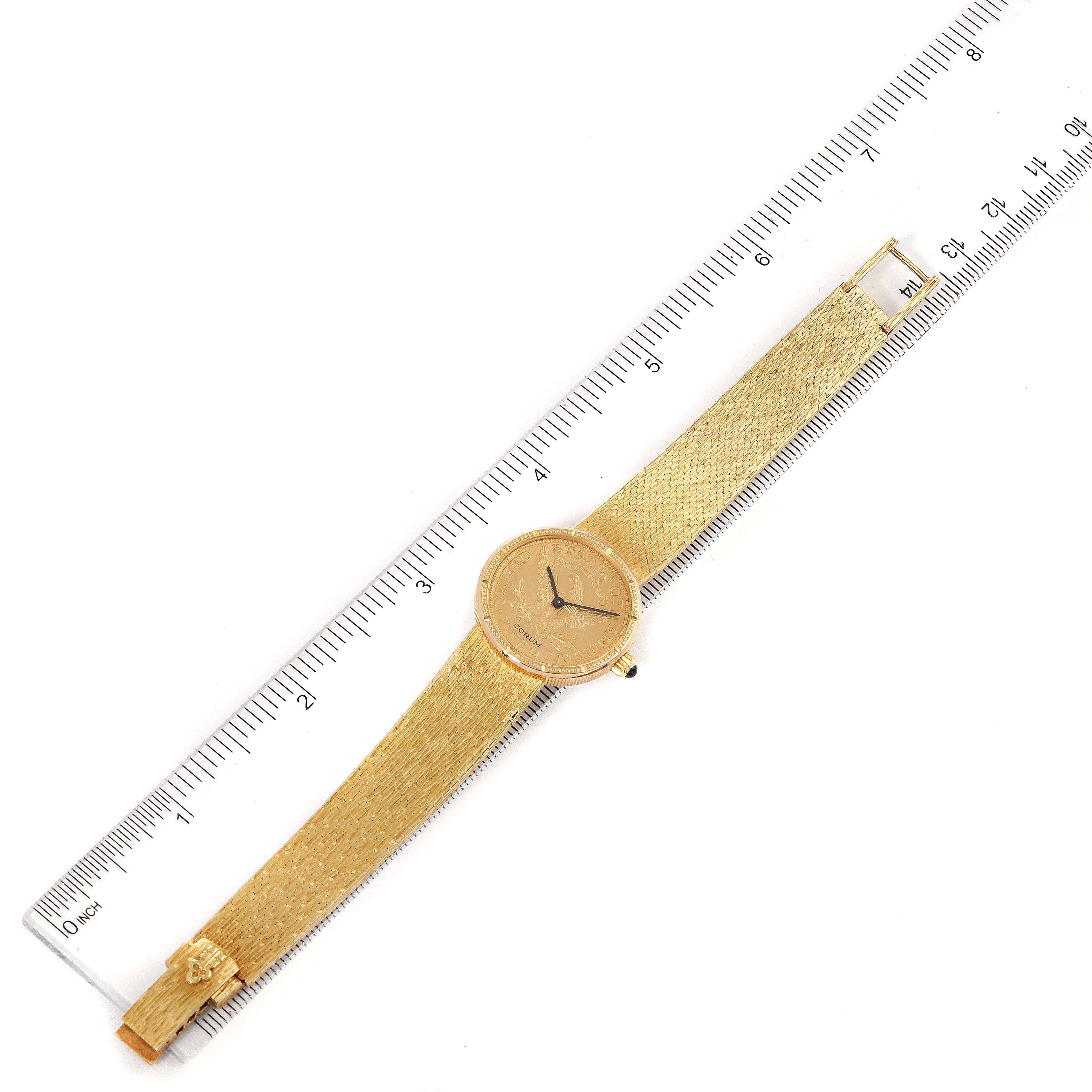 The Coin 5 Dollars Double Eagle Yellow Gold Ladies Watch 1902 model by Corum 1902 Women's Yellow Gold Black Dial 1902 Women's Yellow Gold Black Dial is shown from a top-down angle alongside a ruler for scale.