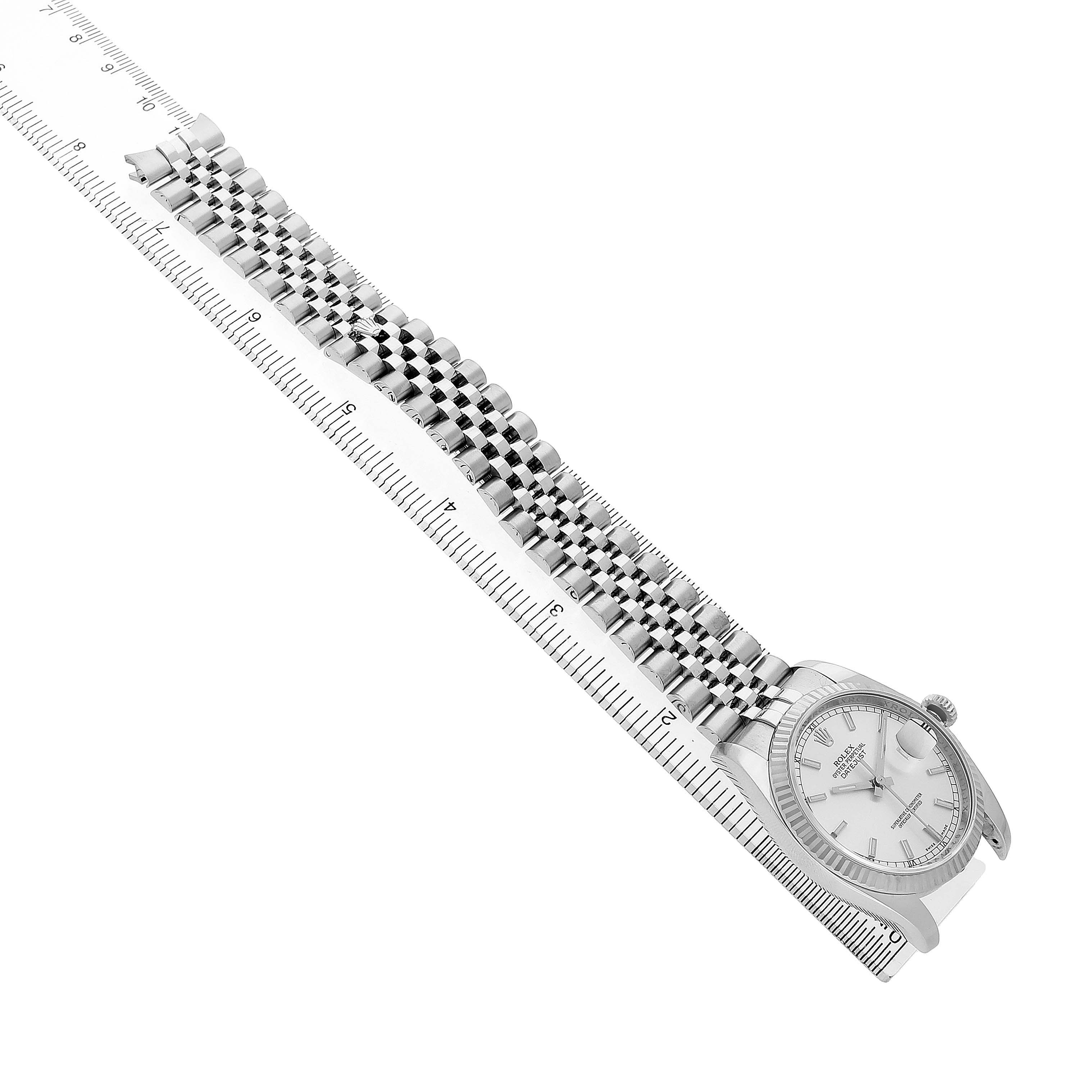 The Rolex Datejust 116234 Men's Stainless Steel Silver Dial watch is shown at a side angle with a focus on its bracelet and case, placed next to a ruler for scale.