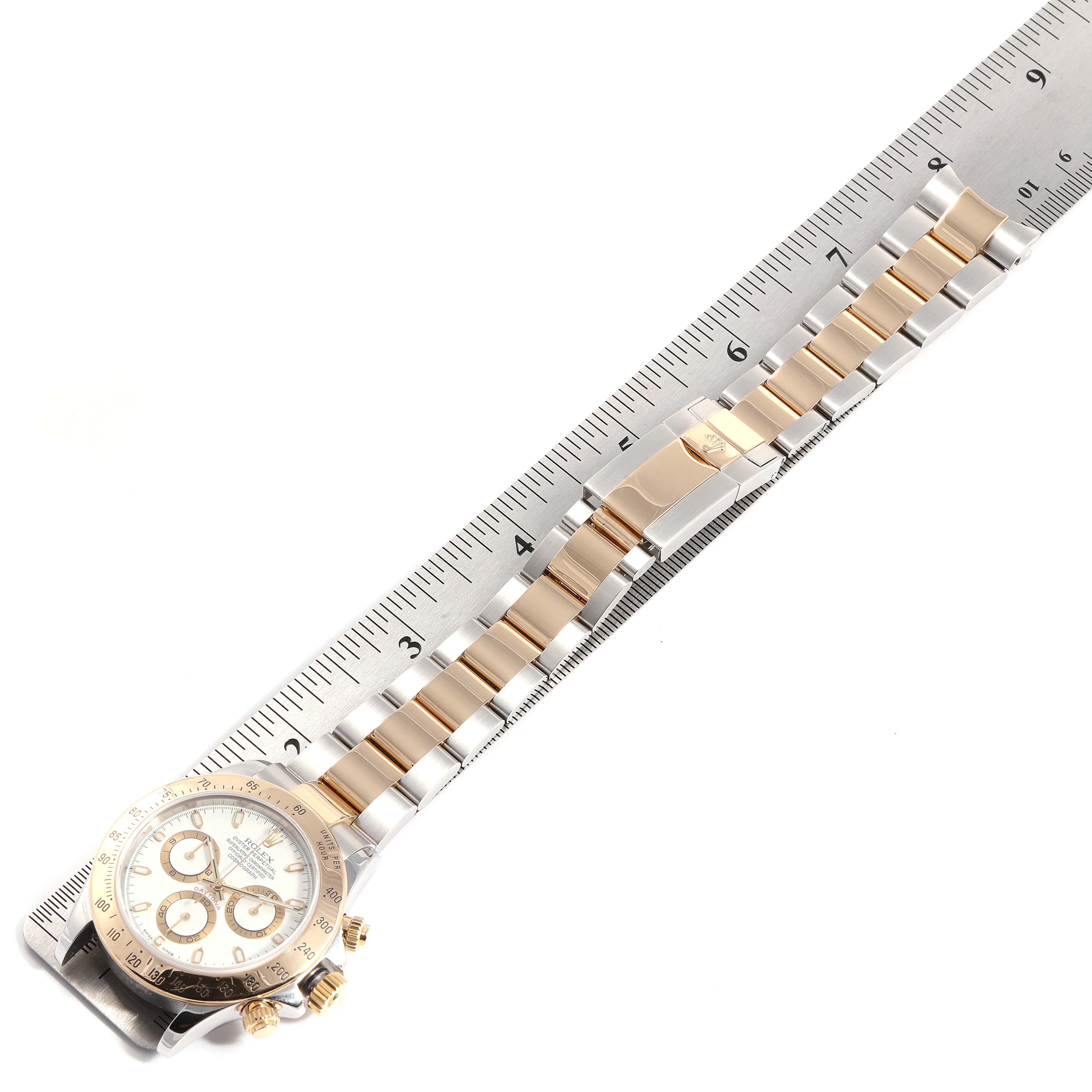 The image depicts the Rolex Daytona 116523 Men
s Steel and Gold (two tone) White Dial 116523 Men
s Steel and Gold (two tone) White Dial watch laid flat on a ruler, showing the face, bezel, and full bracelet from an overhead angle.