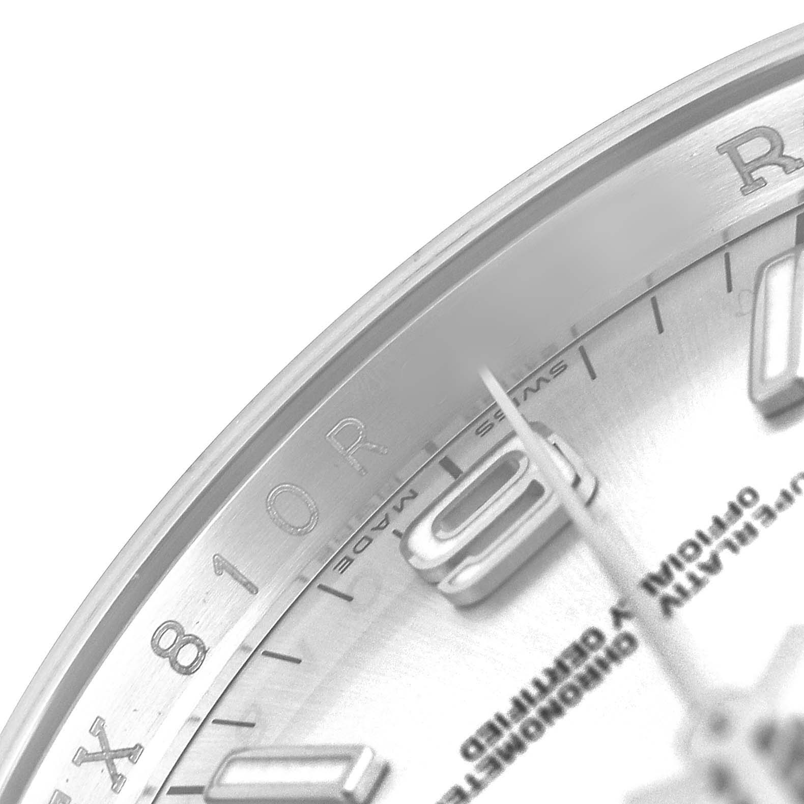 The image shows a close-up of the dial and bezel of a Rolex Oyster Perpetual 116000 Men's Stainless Steel Silver Dial watch, highlighting parts of the indices and text.