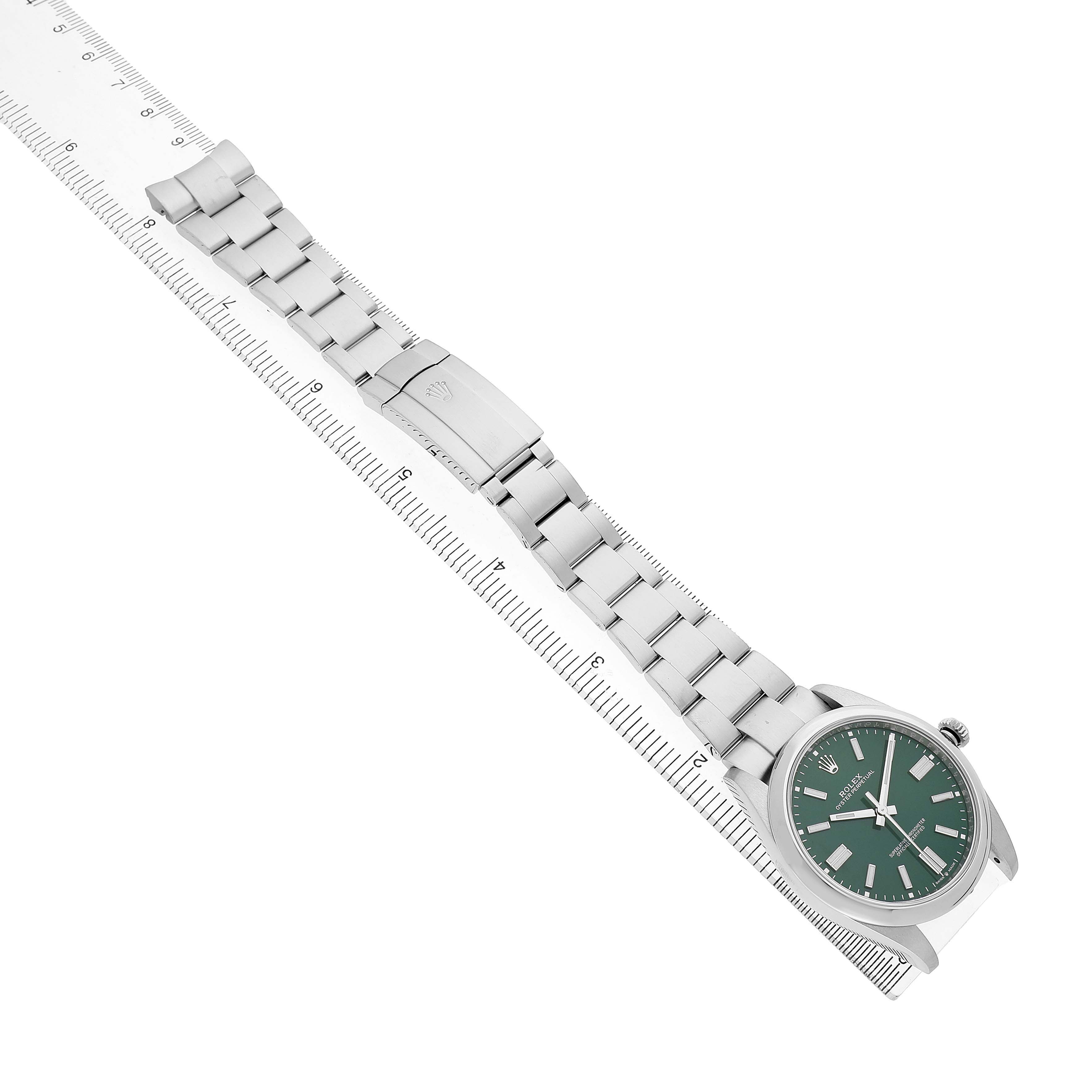 The Rolex Oyster Perpetual M124300-0005 Men's Stainless Steel Green Dial watch is shown from a top angle, highlighting the dial, bracelet, and clasp alongside a ruler for scale.
