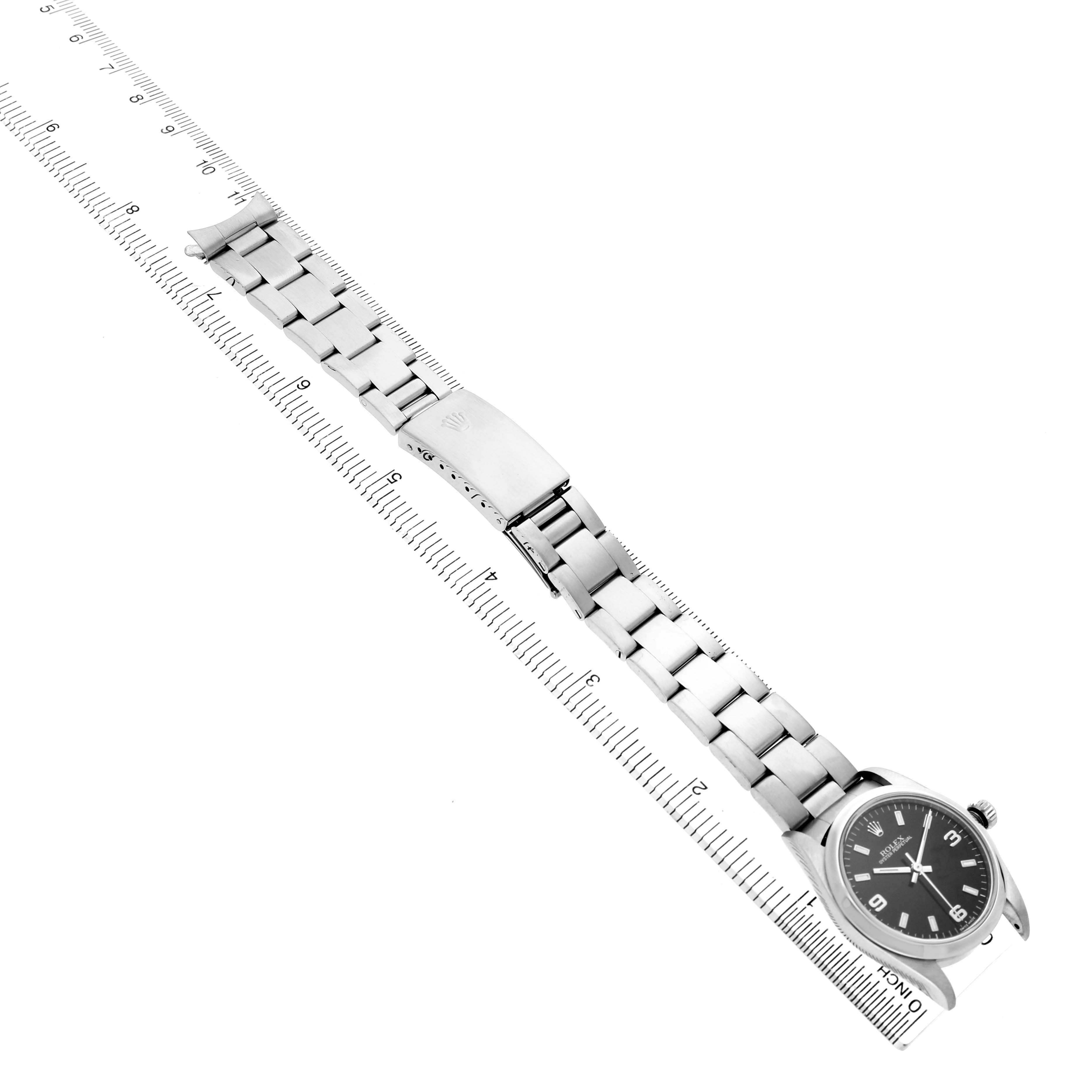 The Rolex Oyster Perpetual 77080 Women's Stainless Steel Black Dial watch is shown from a top-down angle, displaying the face, bracelet, and clasp alongside a ruler.