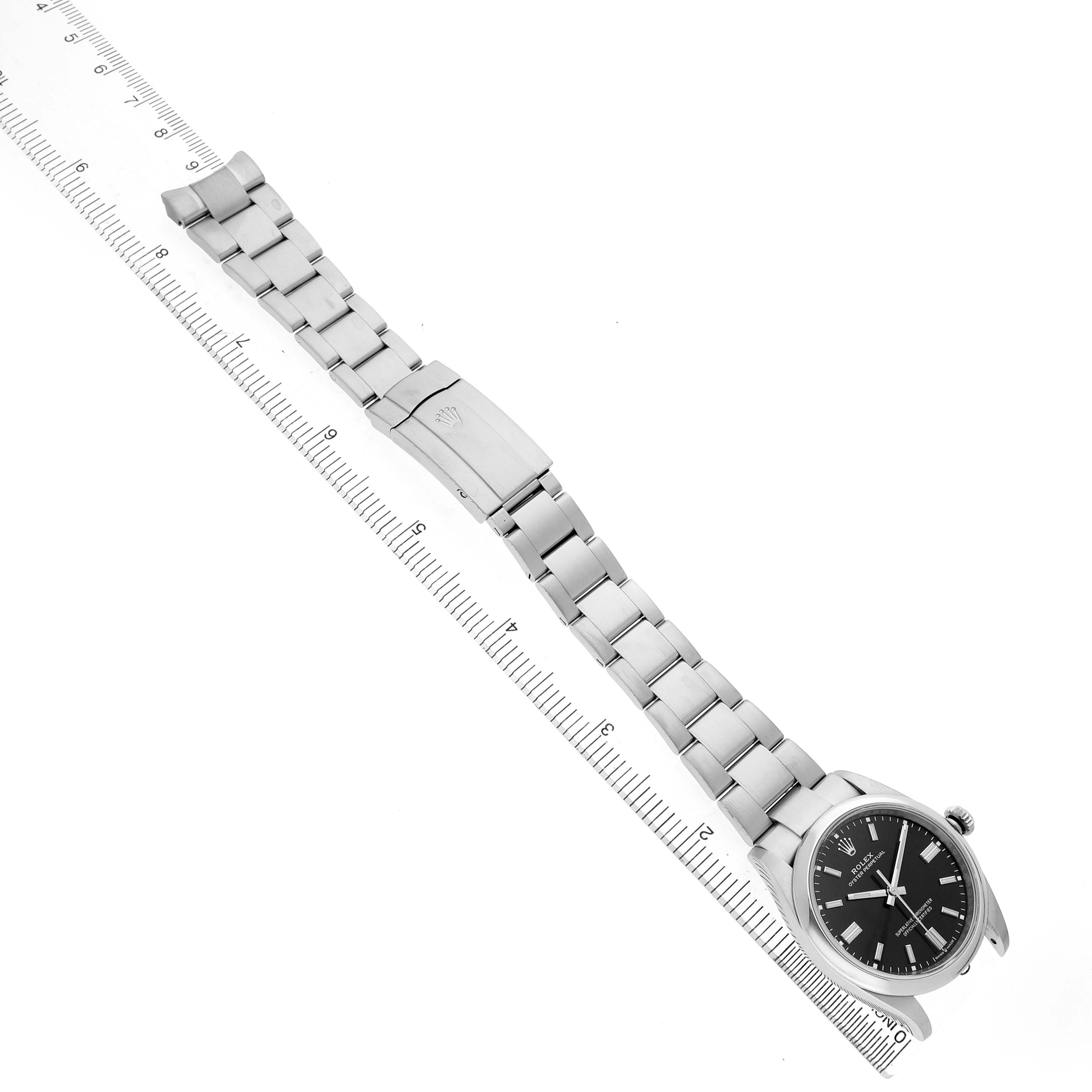 The Rolex Oyster Perpetual 126000 Men's Stainless Steel Black Dial watch is shown from a top view, highlighting the full bracelet and clasp alongside a ruler for scale.