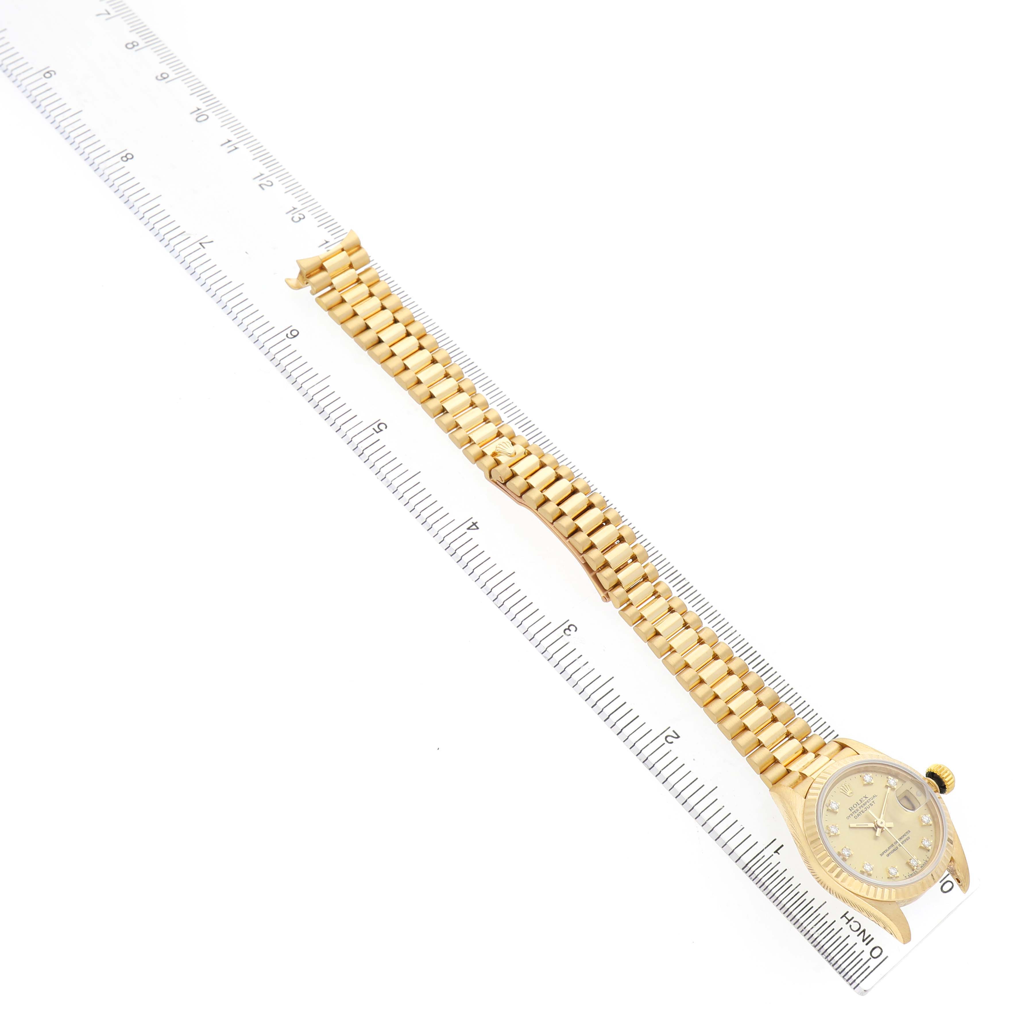 The Rolex President 69178 Men's Yellow Gold Champagne Dial model watch is shown from a top-down angle, displaying its full gold bracelet and dial alongside a ruler.