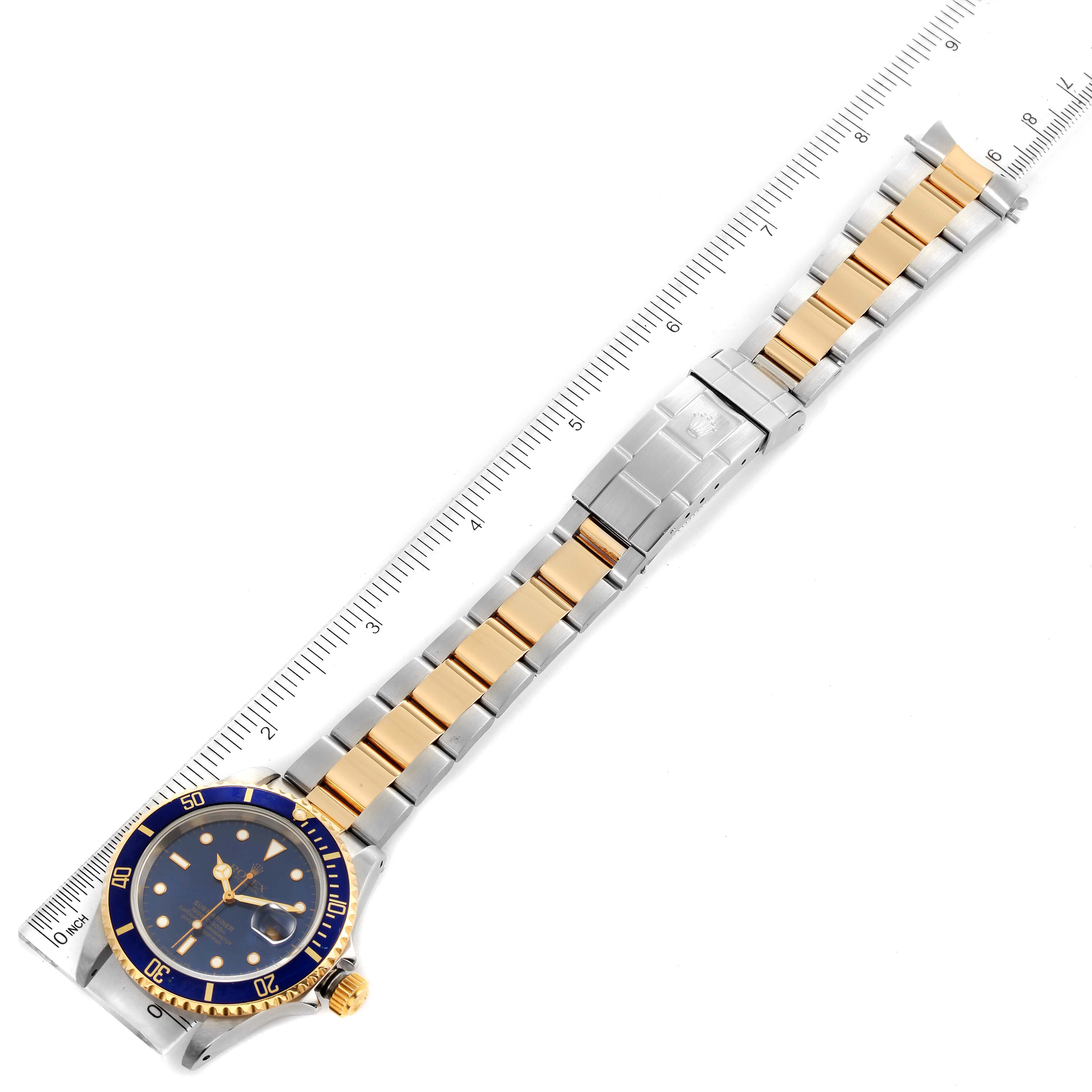 The image shows a top-down view of a Rolex Submariner 16613 Men
s Steel and Gold (two tone) Blue Dial 16613 Men
s Steel and Gold (two tone) Blue Dial watch, including its blue and gold bezel and two-tone bracelet, measured against a ruler.