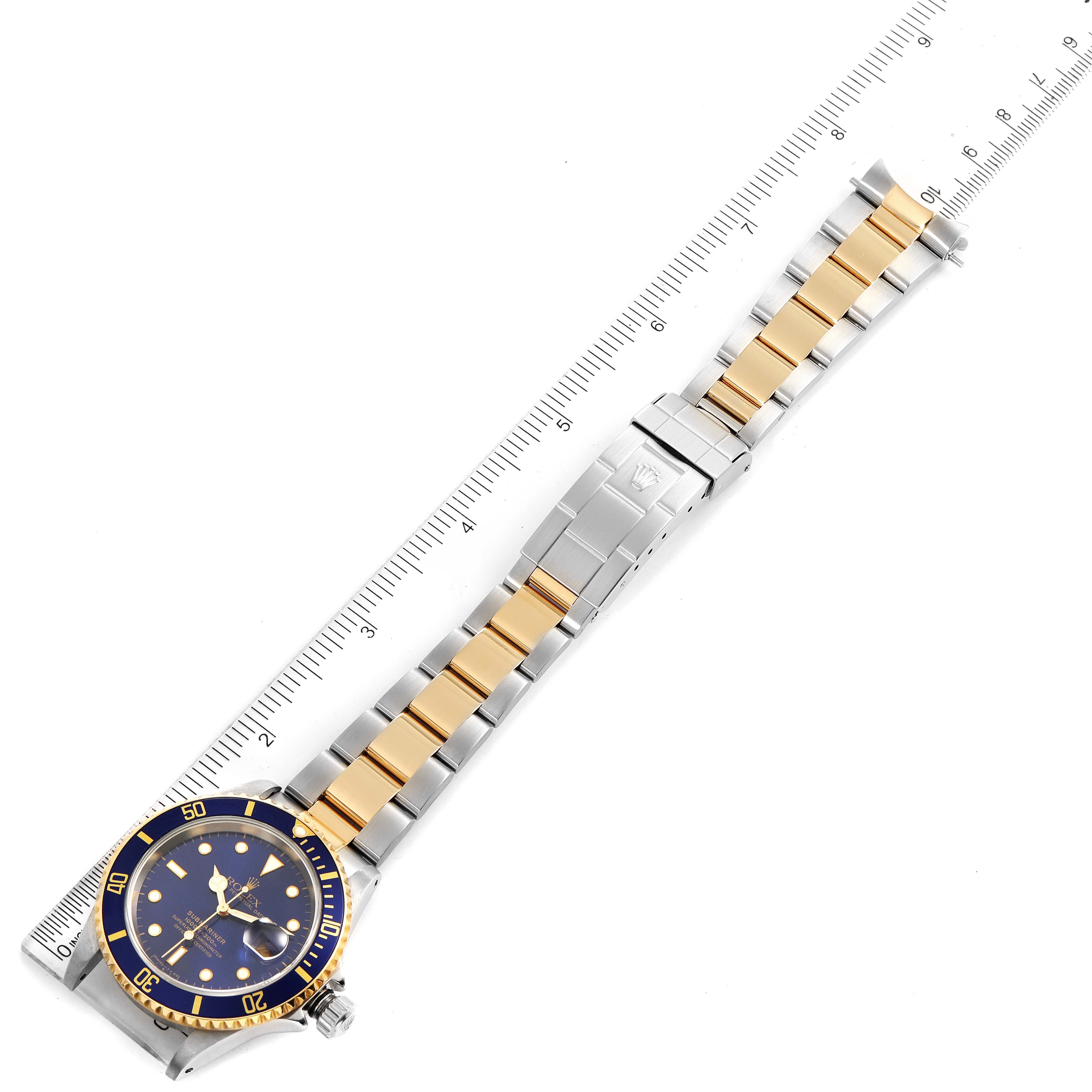 The image shows a top-angle view of a Rolex Submariner 16613 Men
s Steel and Gold (two tone) Blue Dial 16613 Men
s Steel and Gold (two tone) Blue Dial watch, showcasing its blue dial and two-tone gold and silver bracelet, alongside a ruler for scale.