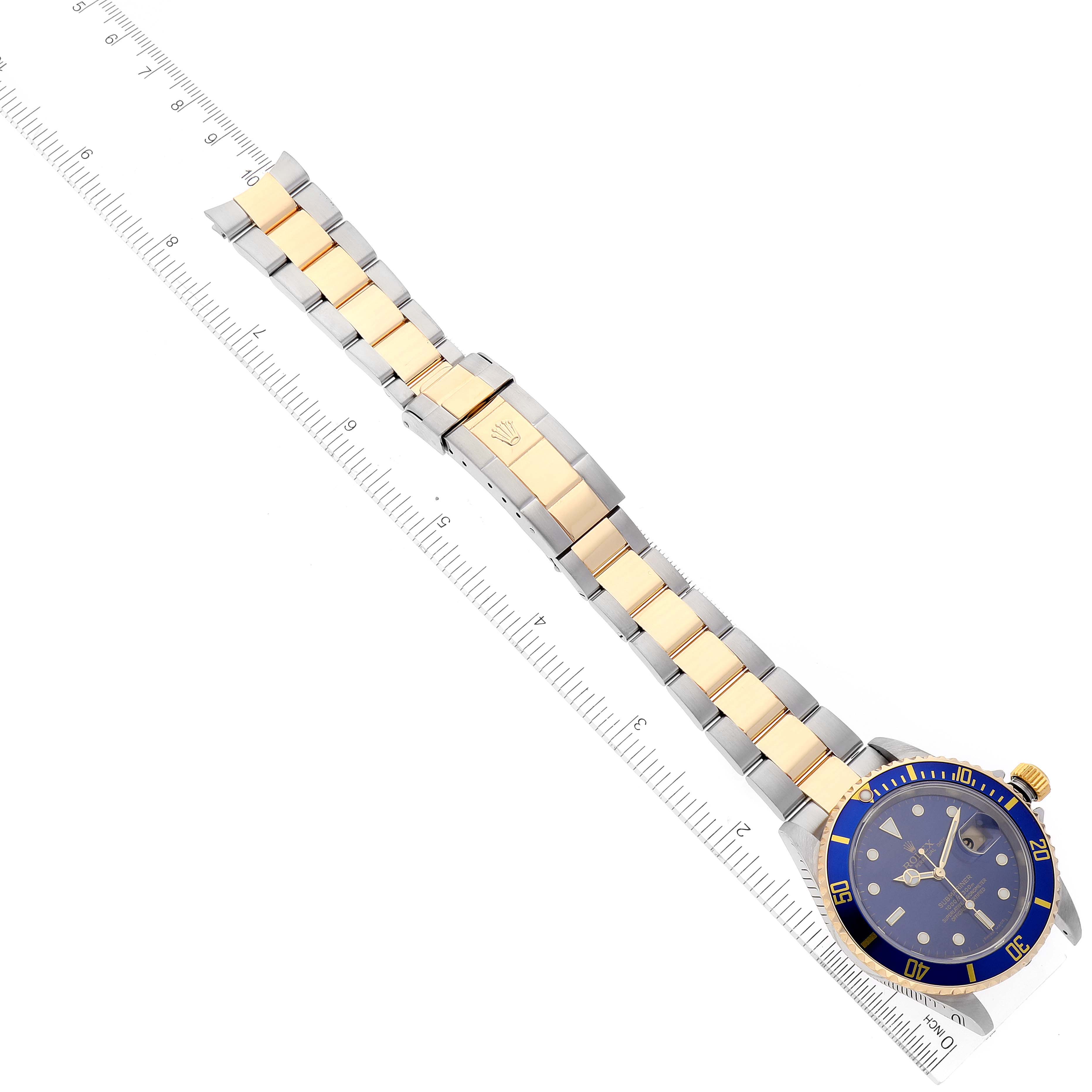 The image shows a top-down view of a Rolex Submariner 16613 Men's Steel and Gold (two tone) Blue Dial 16613 Men's Steel and Gold (two tone) Blue Dial watch, including its face and bi-metal bracelet, placed next to a ruler.