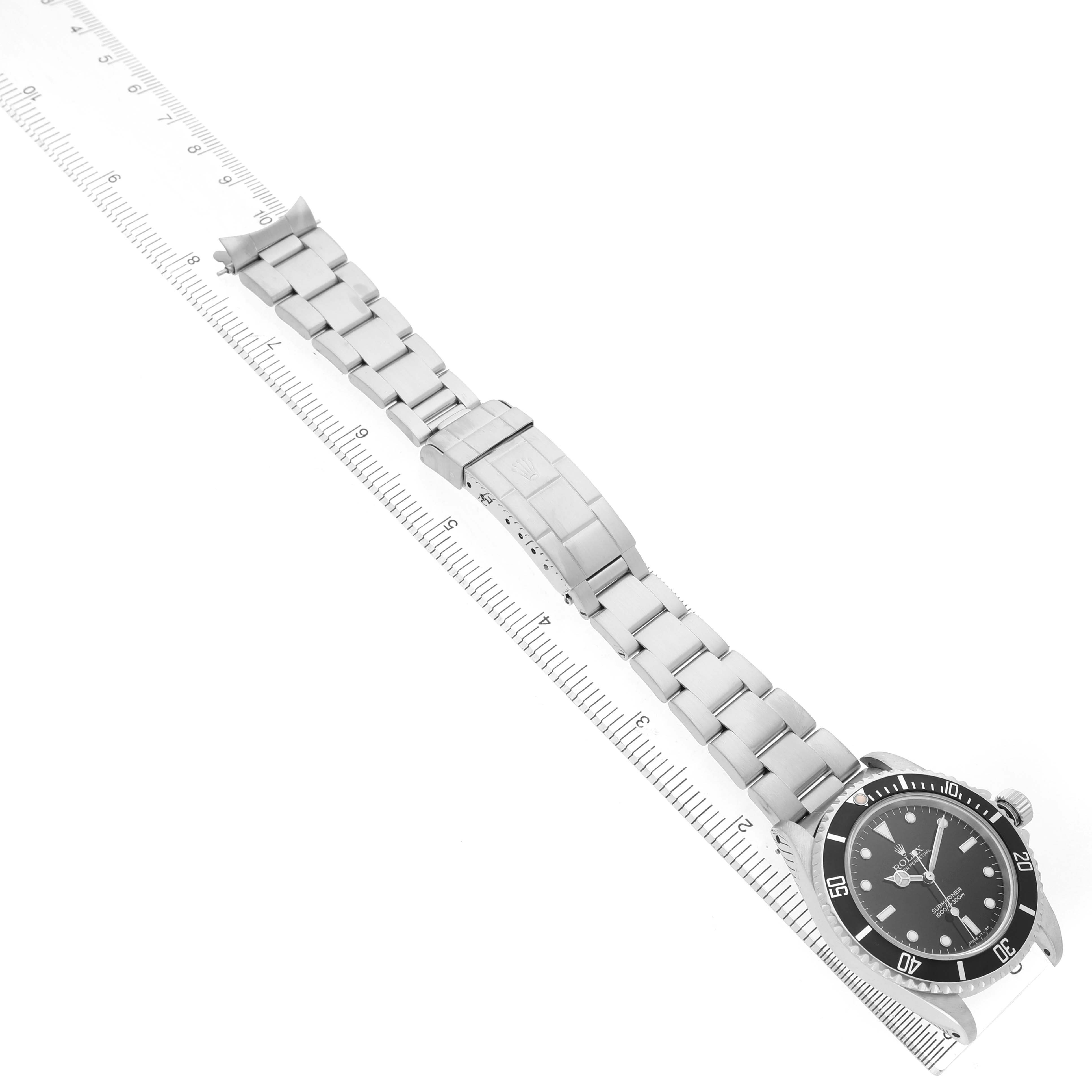 The Rolex Submariner 14060M Men's Stainless Steel Black Dial watch is shown from a top-down angle, displaying the bracelet fully extended alongside a ruler.